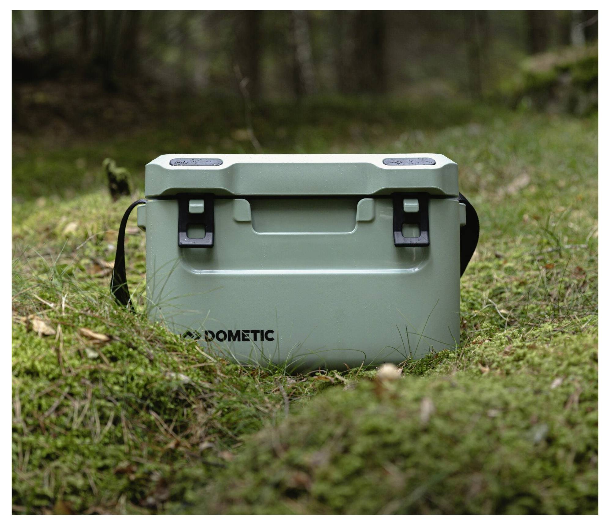 Mintgrüne Dometic-Kühlbox, die auf Gras in einer bewaldeten Außenumgebung steht.