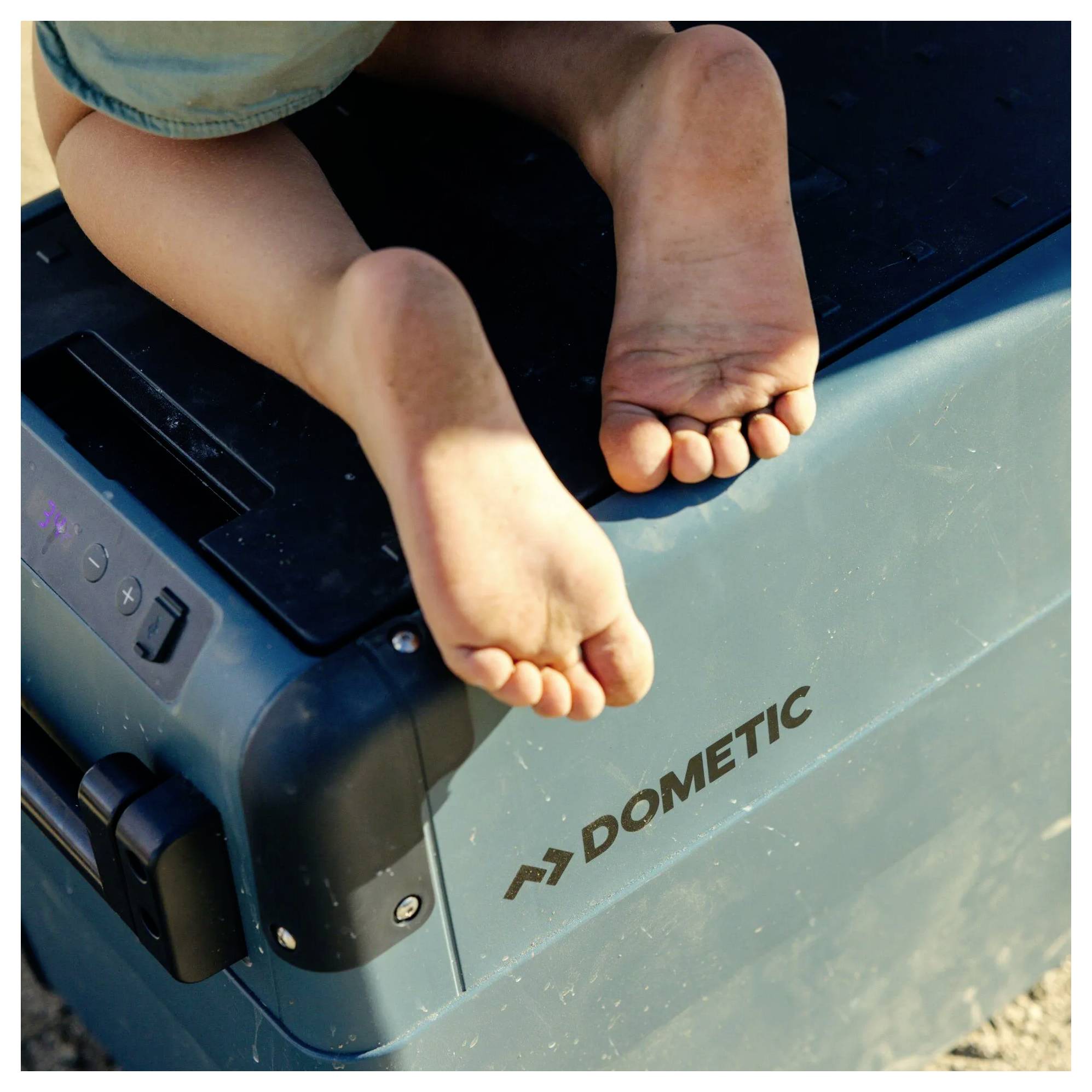 Barfüße ruhen auf einer blauen Dometic-Kühlbox oder einem Gerät, aus der Nähe im Freien fotografiert.