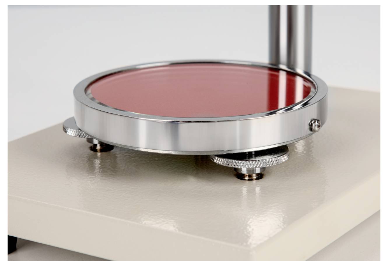 Eine Nahaufnahme eines wissenschaftlichen Instruments mit einer roten kreisförmigen Platte und einstellbaren Metallknöpfen, wahrscheinlich zur Durchführung von Messungen oder Experimenten verwendet.