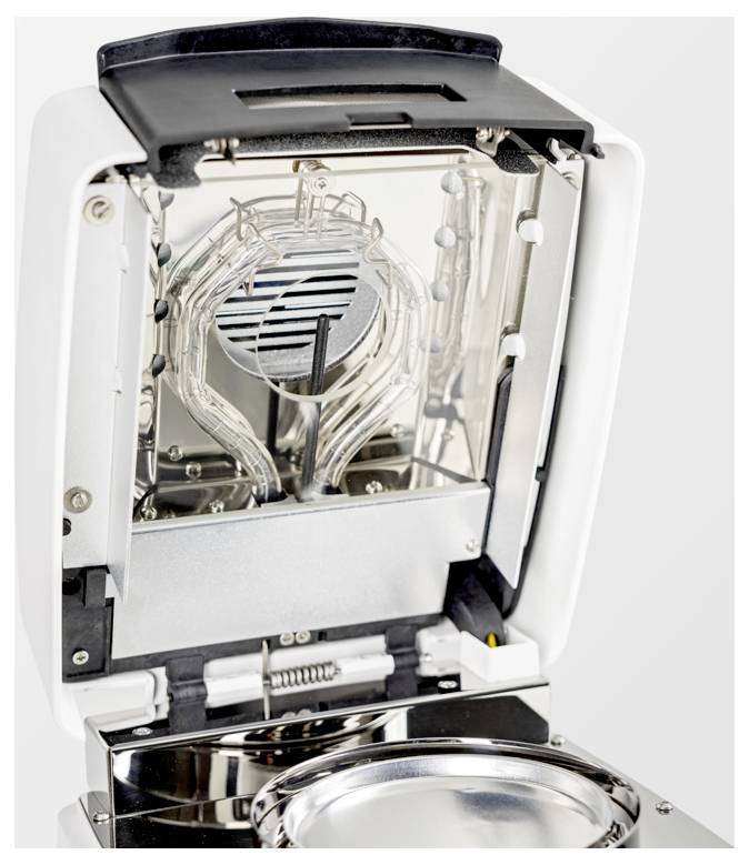 Offene Ansicht eines modernen Geräts mit einem reflektierenden Innenraum und einer runden metallischen Plattform, die technische Komponenten im Inneren zeigt.