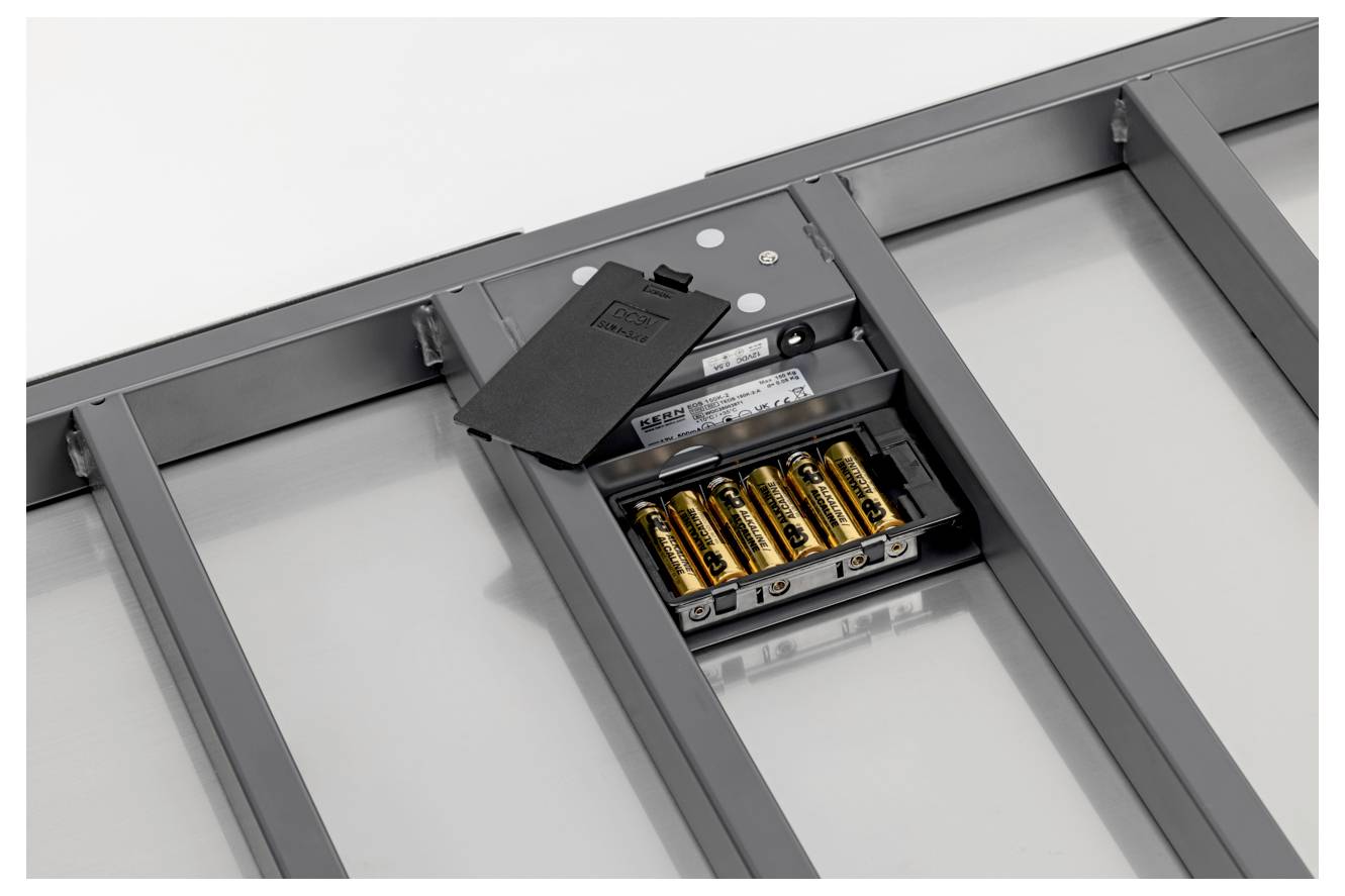 Das Bild zeigt die Rückseite eines kleinen weißen elektronischen Geräts mit acht sichtbaren Schrauben.