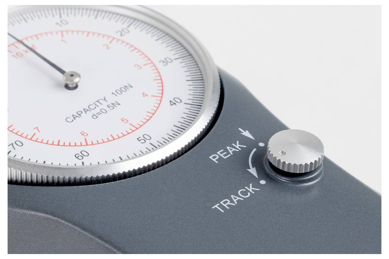 Eine Nahaufnahme einer mechanischen Scheibenmanometer-Anzeige mit Messwerten. Ein Drehknopf mit den Beschriftungen 
