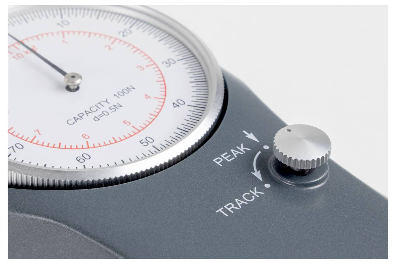 Eine Nahaufnahme eines analogen Kraftmessers, der eine Messskala von 0 bis 100N, einen Knopf mit den Einstellungen 