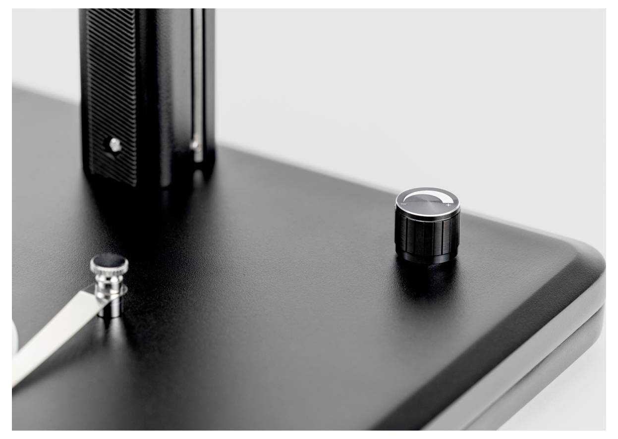 Eine Nahaufnahme eines eleganten, modernen Plattenspielers, die den Tonarm und den metallischen Bedienknopf auf einer schwarzen matte Oberfläche hervorhebt.