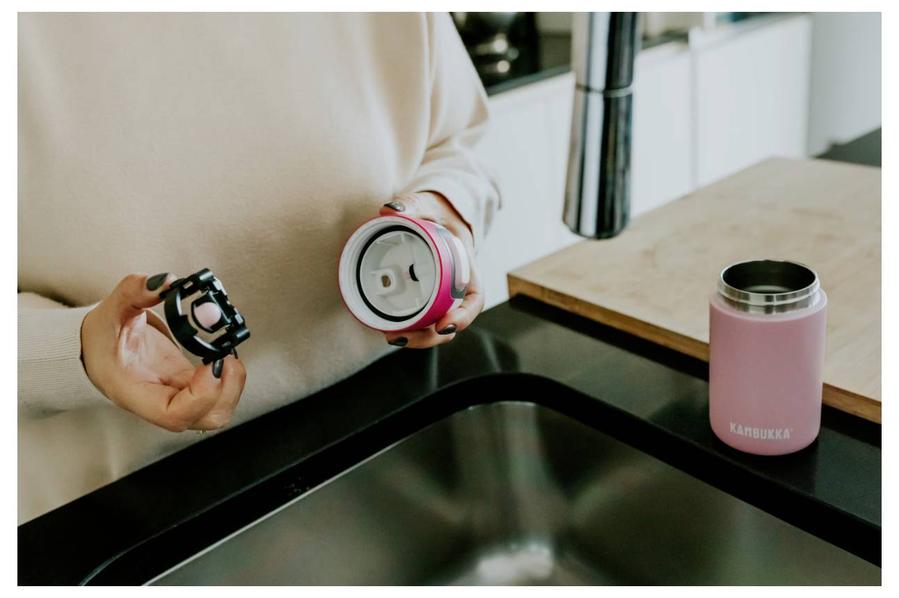 Eine Person an einer Küchenspüle hält zerlegte Teile eines rosa Trinkbechers, während der Boden in der Nähe auf einer schwarzen Arbeitsplatte sitzt.