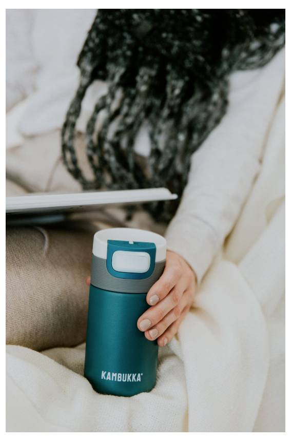 Eine Person sitzt auf einem Sofa, hält einen türkisfarbenen isolierten Becher mit der Aufschrift 