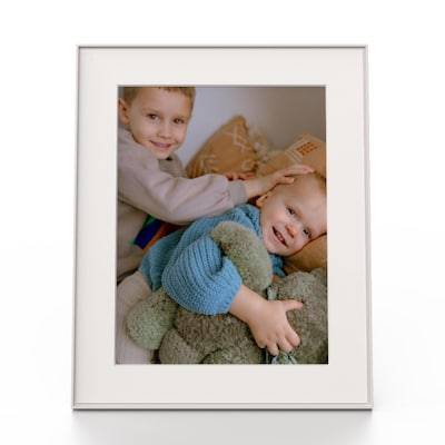 Zwei junge Kinder lächeln, eines trägt eine Pappkrone. Das jüngere Kind hält ein großes Plüschtier. Sie sind drinnen und sitzen eng beieinander.