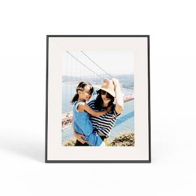 Ein gerahmtes Foto zeigt eine Person mit einem Hut, die ein Kind hält, mit der Golden Gate Bridge im Hintergrund an einem sonnigen Tag.