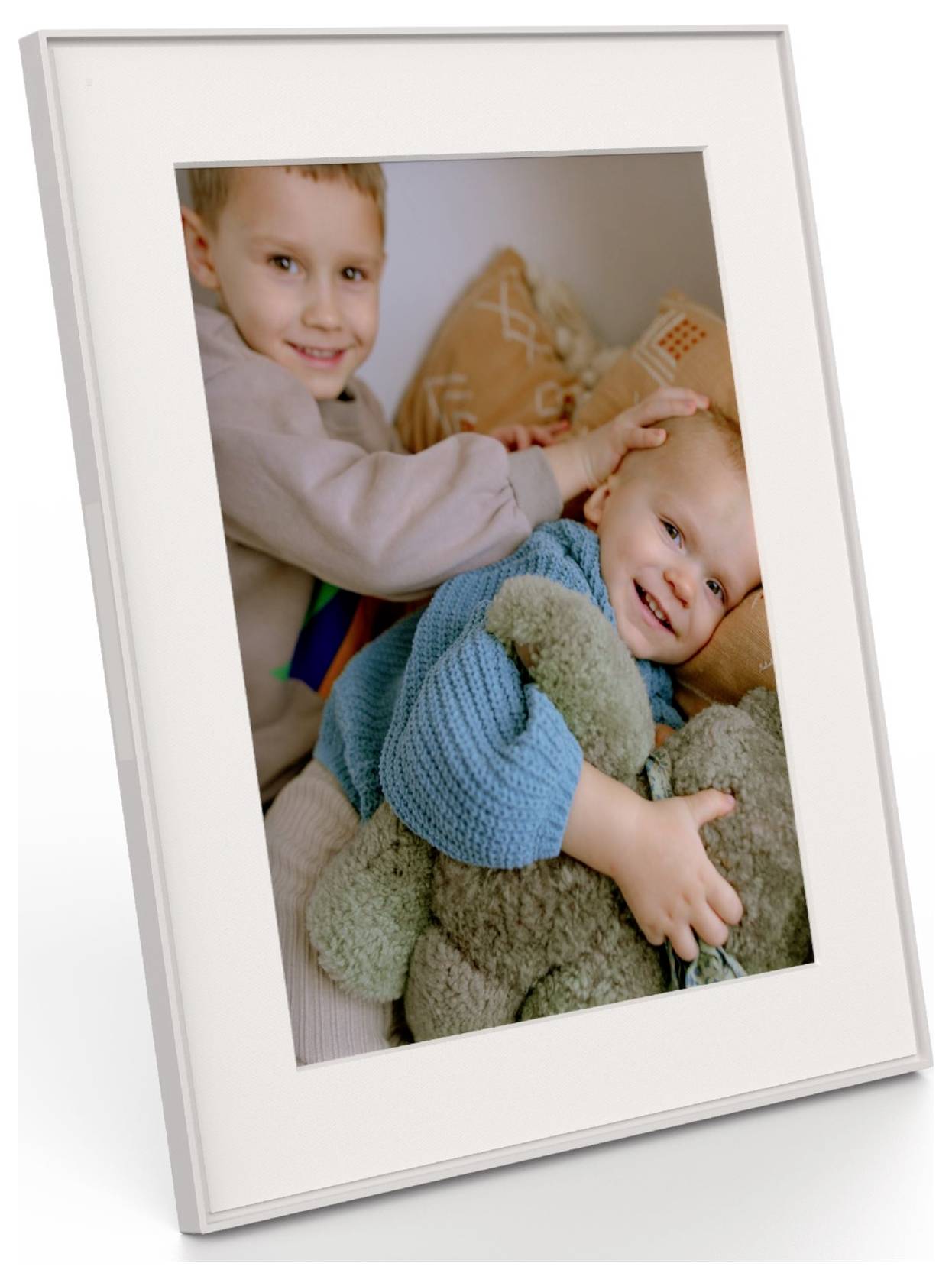 Zwei lächelnde Kinder sitzen auf einem Sofa. Das ältere Kind umarmt das jüngere sanft und hält ein Plüschtier, wobei eine warme, fröhliche Szene entsteht.