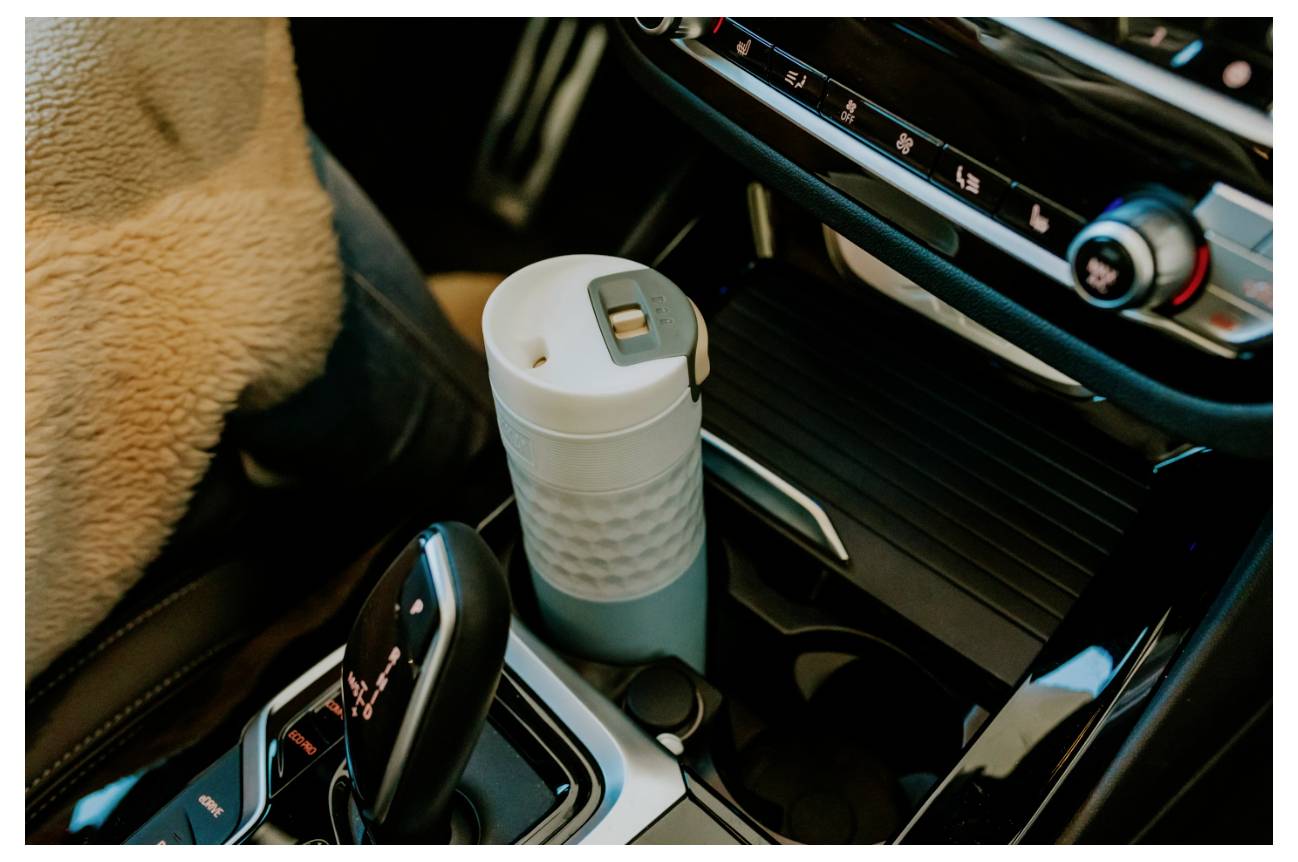 Getränkehalter mit einer wiederverwendbaren Reisebecher in der Mittelkonsole eines Autos neben der Gangschaltung, umgeben von eleganten Bedienungselementen des Armaturenbretts.