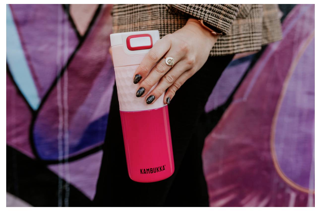 Eine Person, die eine rote Reisekaffeetasse mit dem Label „Kambukka