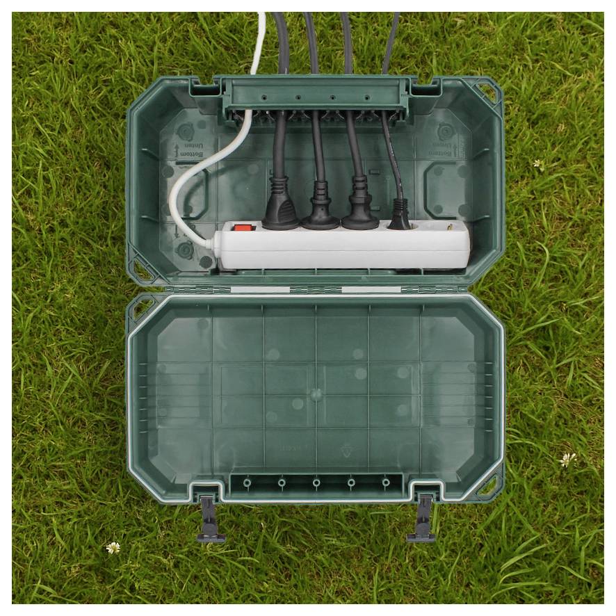 Eine grüne wasserdichte Außensteckdosenbox mit einer Steckdosenleiste mit mehreren angeschlossenen Steckern, auf Gras platziert.