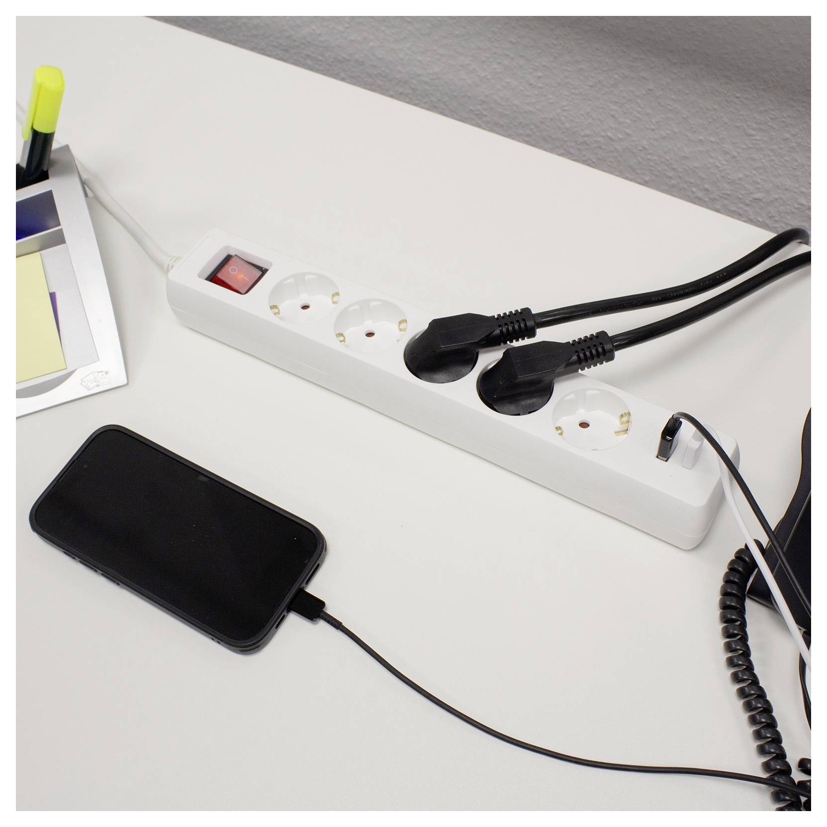 Telefonladung über eine Steckerleiste auf einem Schreibtisch mit anderen angeschlossenen Geräten, was ein Arbeitsplatzaufbau anzeigt.