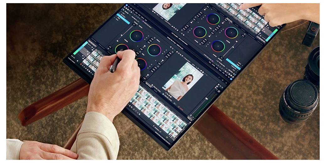 Zwei Personen bearbeiten Fotos an einem Computer mit Doppelbildschirm. Eine Person verwendet einen Stift, eine andere zeigt auf den Bildschirm. In der Nähe befinden sich Kameraobjektive.