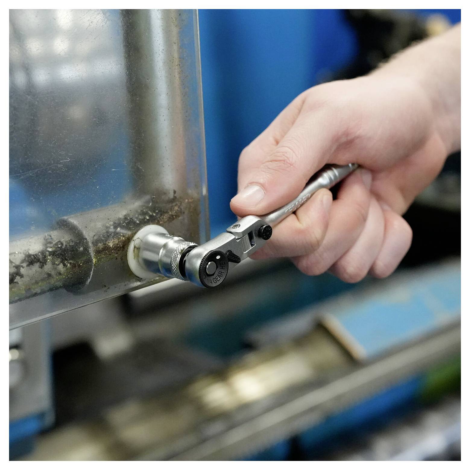 Nahaufnahme einer Hand, die einen Ratschenschlüssel verwendet, um eine Metallarmatur an einer Industriemaschine festzuziehen.