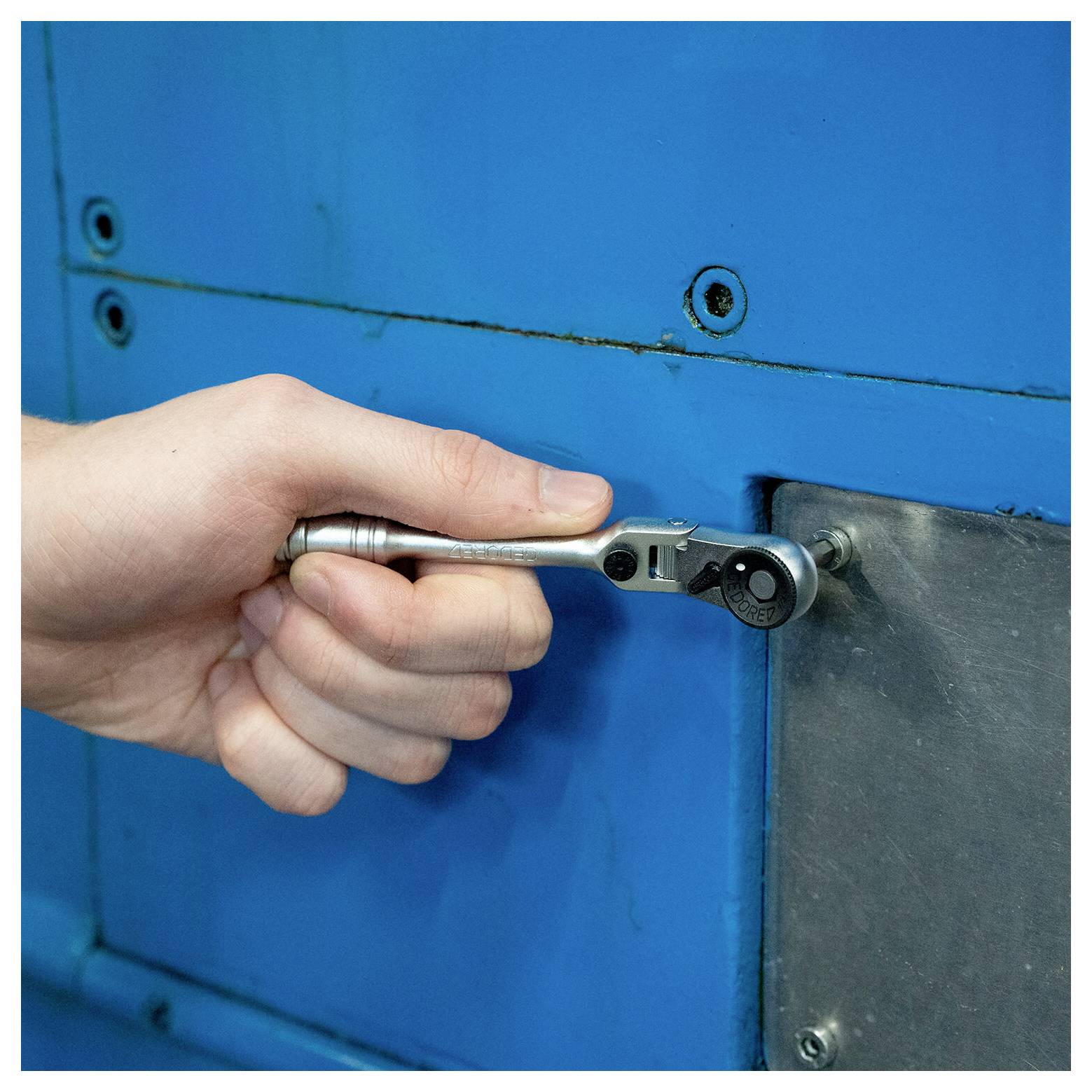 Hand mit einem Ratschenschlüssel zum Festziehen einer Schraube auf einem blauen Metallmaschinenpanel.