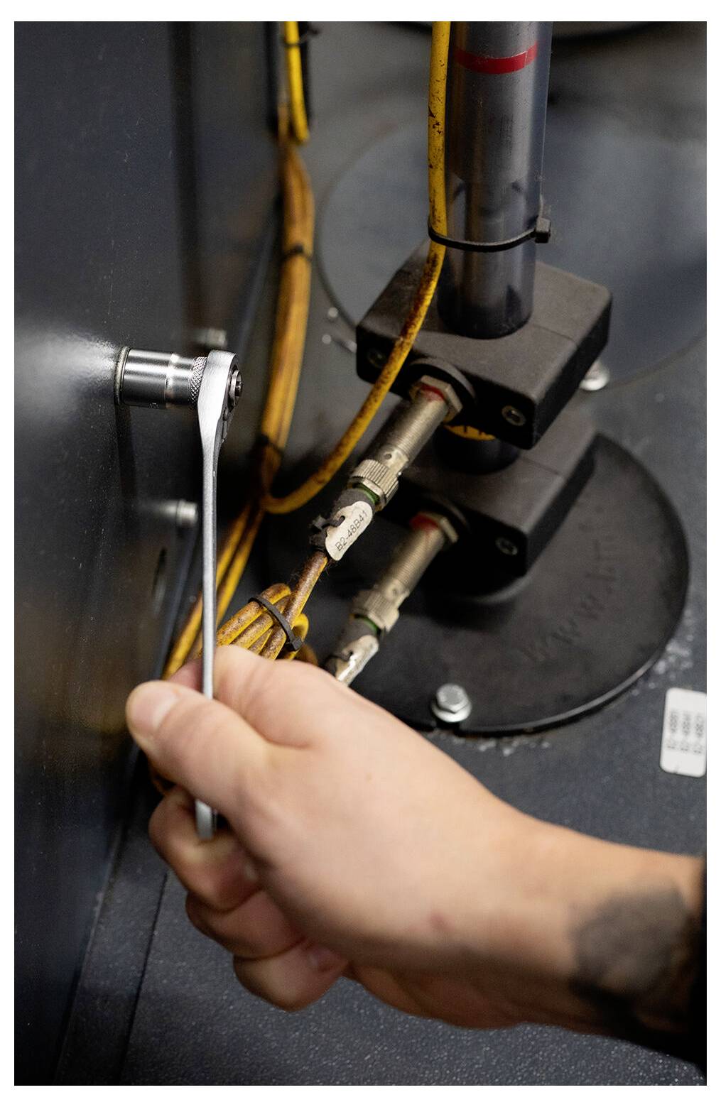 Eine Hand benutzt einen Schraubenschlüssel, um Verbindungsstücke an Industrierohren und Ventilen in einem Maschinen- oder Ausrüstungsschrank festzuziehen.