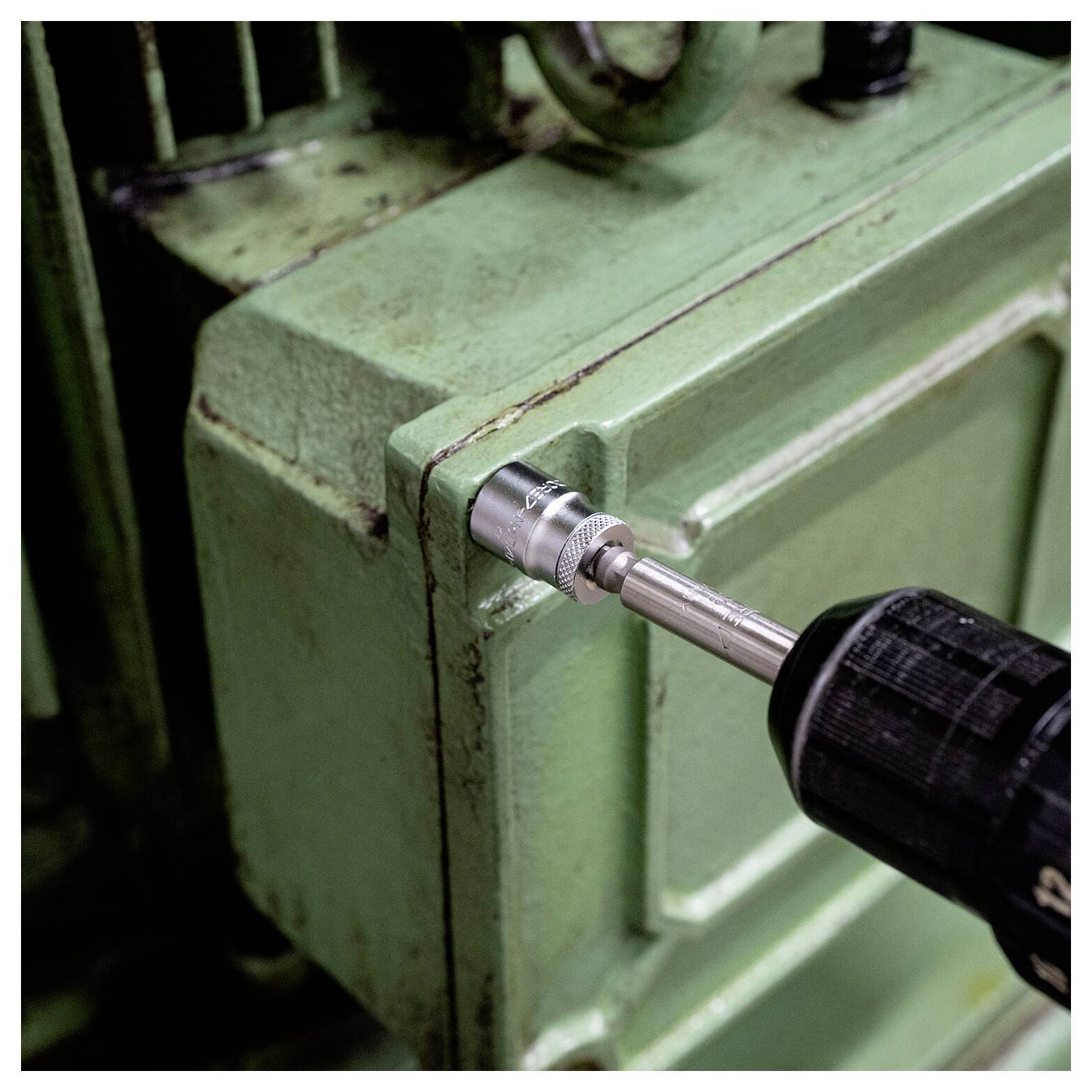 Nahaufnahme eines Bohrers, der eine Befestigung an einem grünen Metallgehäuse einer Maschine anzieht.