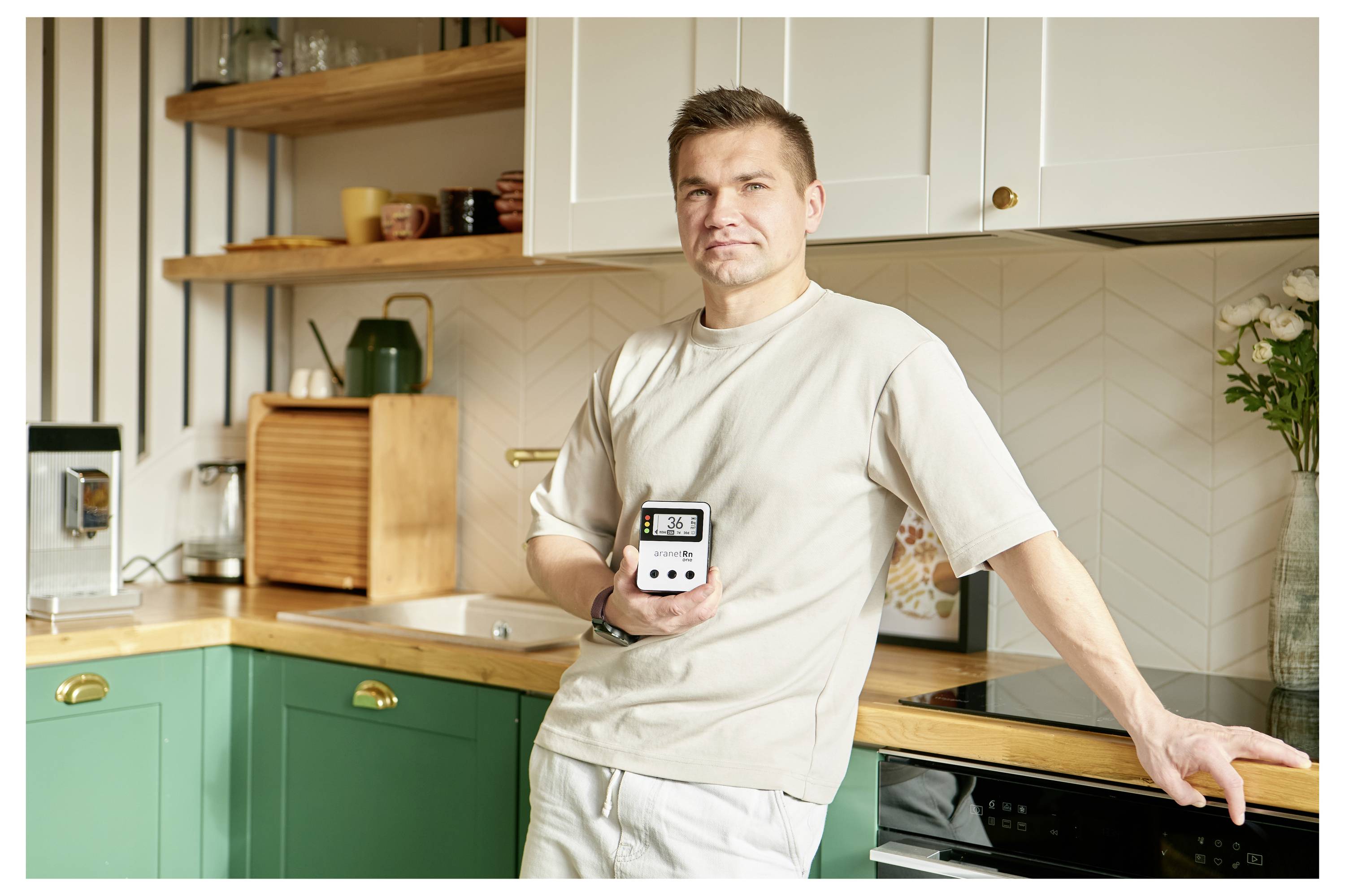 Ein Mann steht in einer Küche und hält ein elektronisches Gerät, das eine Uhrzeit anzeigt.