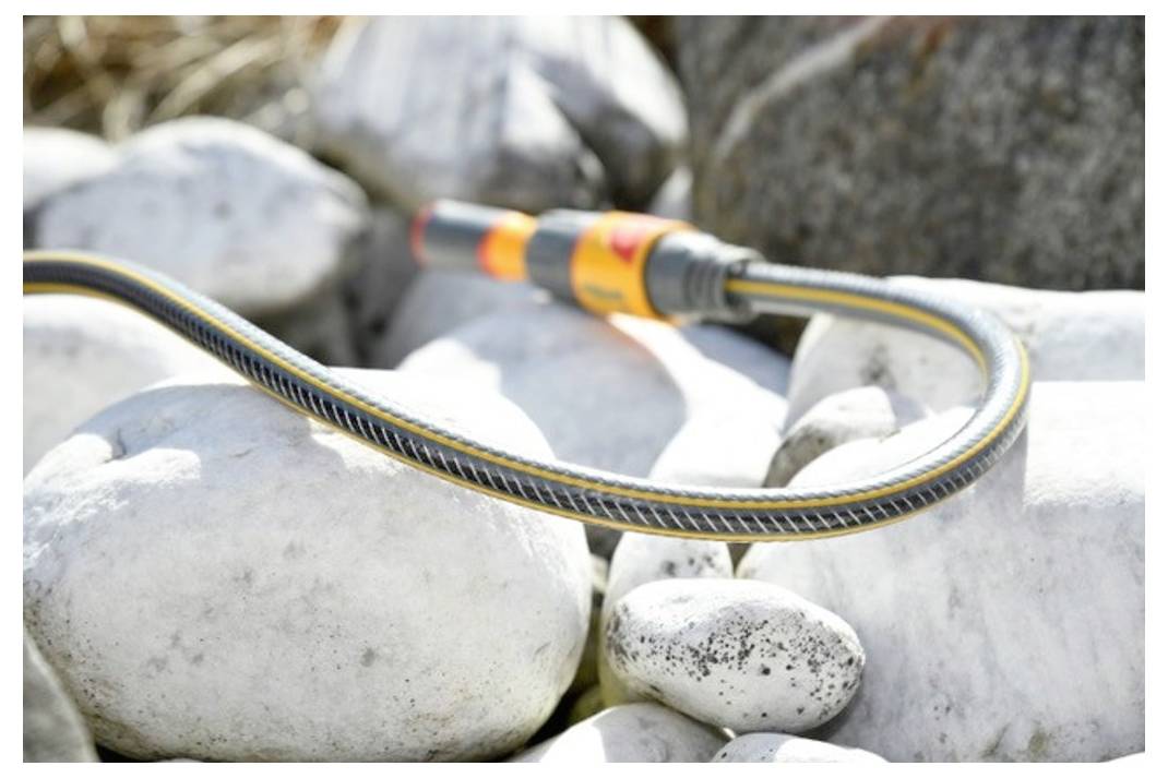 Ein flexibler Schlauch mit einer Düse ruht auf glatten weißen Steinen, möglicherweise in einem Garten oder einer Außenumgebung, was auf eine Bewässerungsnutzung hindeutet.