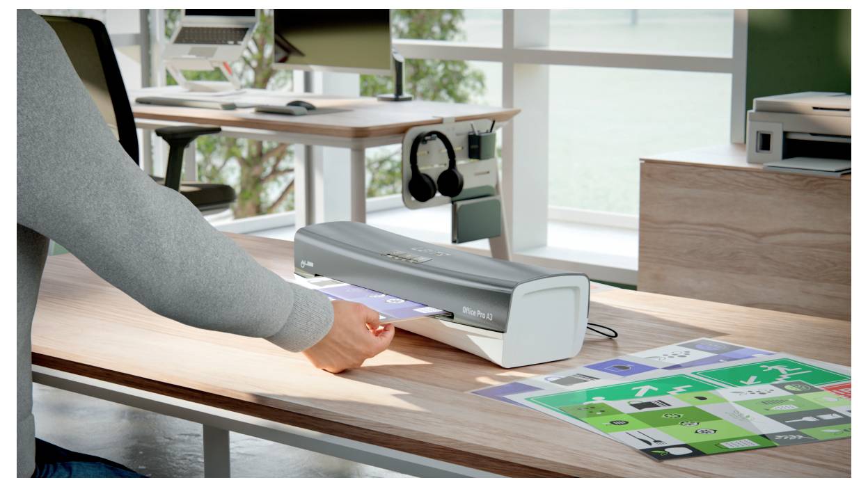 Eine Person laminiert bunte Blätter mit einem Desktop-Laminiergerät auf einem Holztisch in einem Büro mit großen Fenstern und Grün außen.