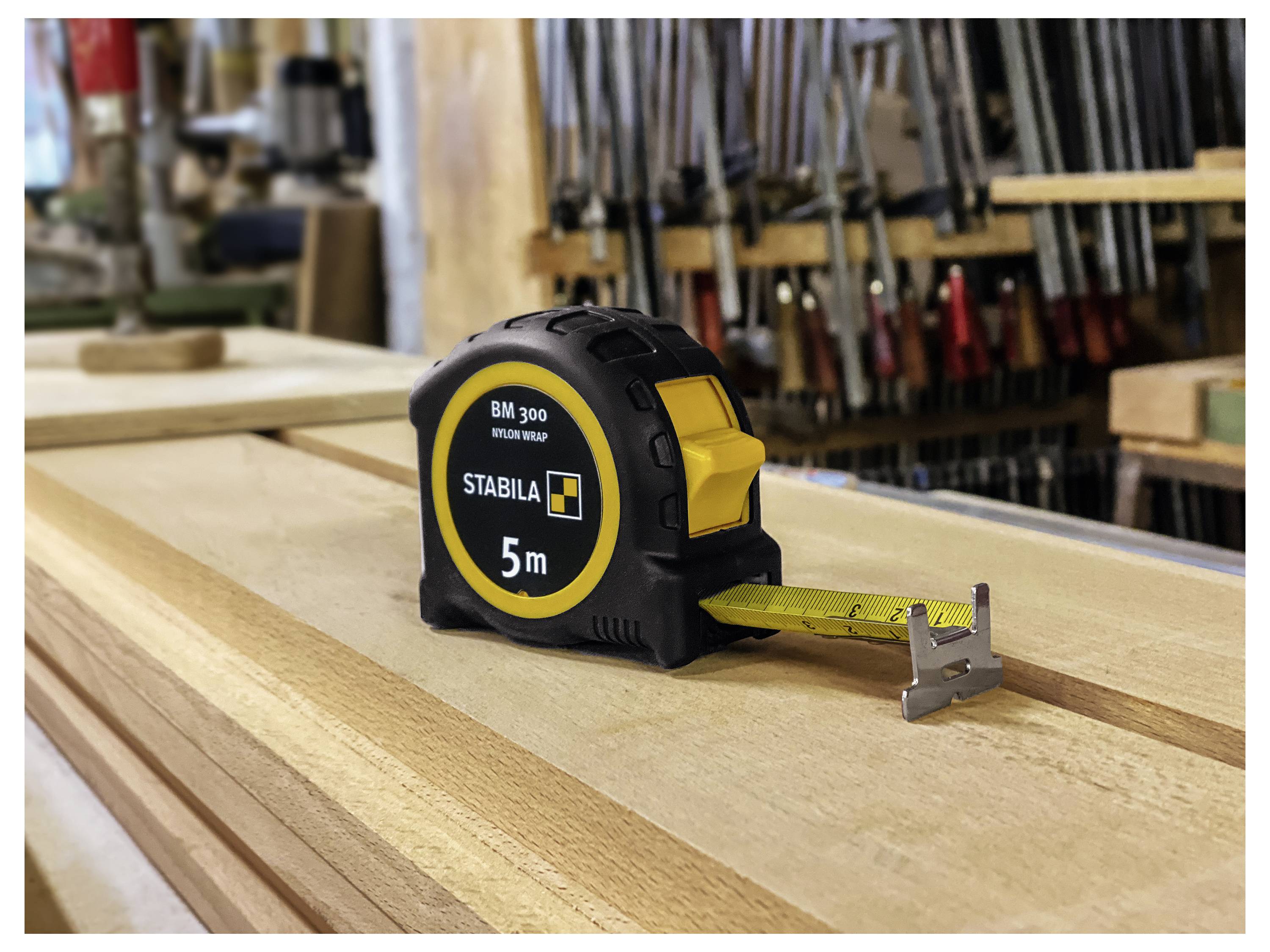 Ein Stahllineal, das auf Holzdielen in einer Werkstatt ruht, mit Werkzeugen, die im Hintergrund sichtbar sind.