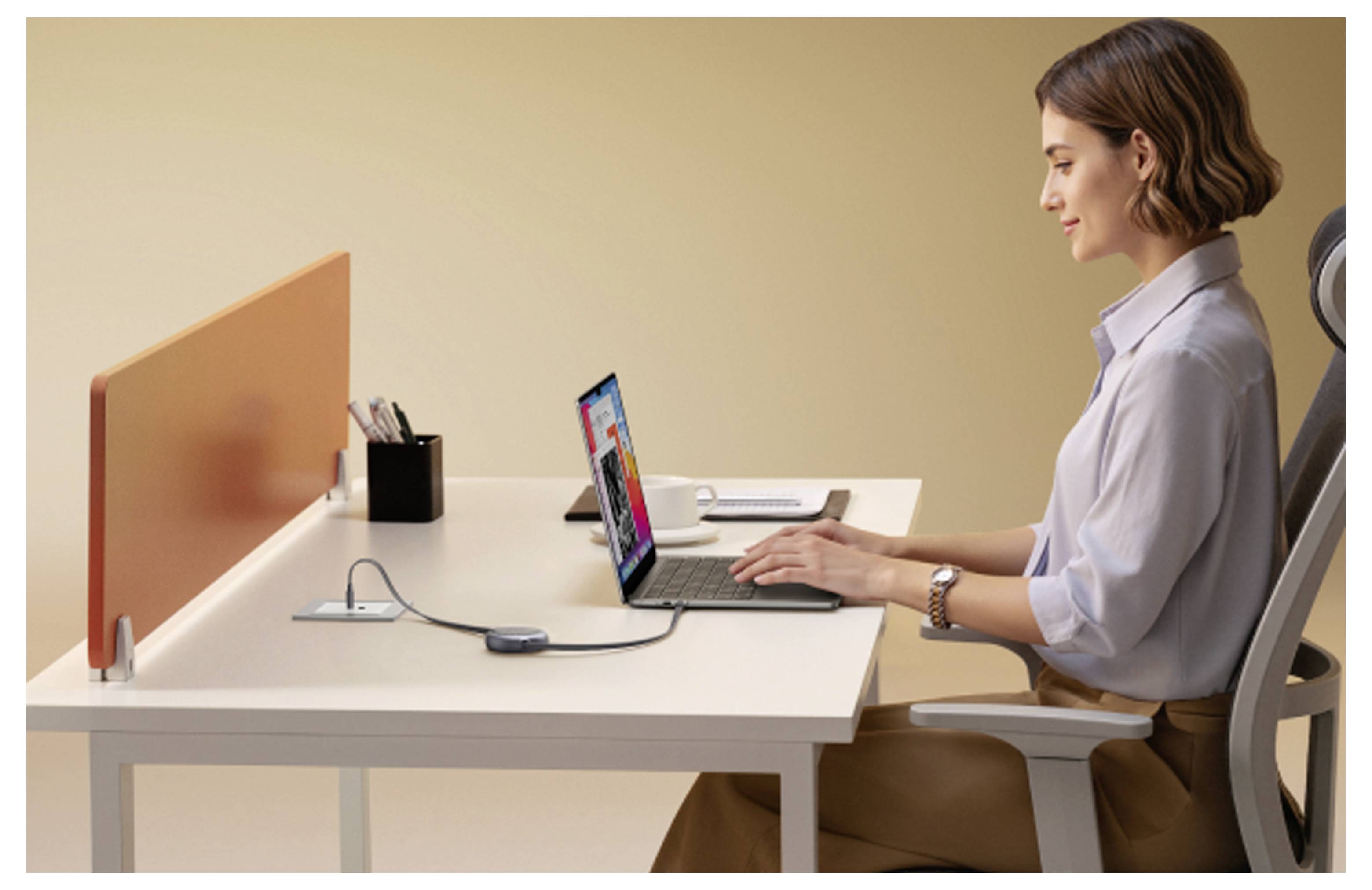 Frau tippt auf einem Laptop an einem Schreibtisch in einem modernen Büro, mit einem orangefarbenen Sichtschutz und Schreibtischartikel in der Nähe.