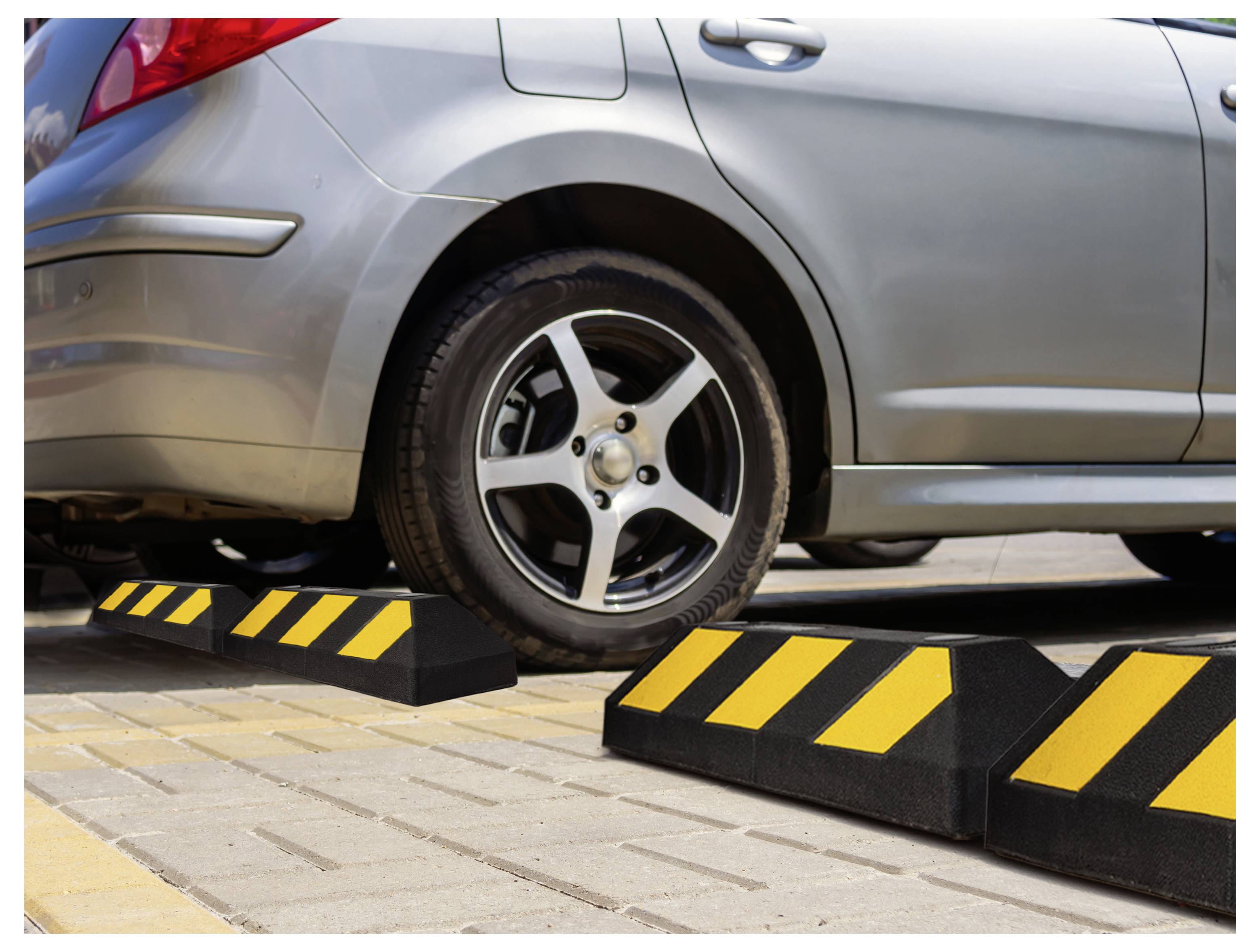 Autorreifen auf einem schwarz-gelben Radstoppstein geparkt, mit einem silbernen Auto auf einem Parkplatz.