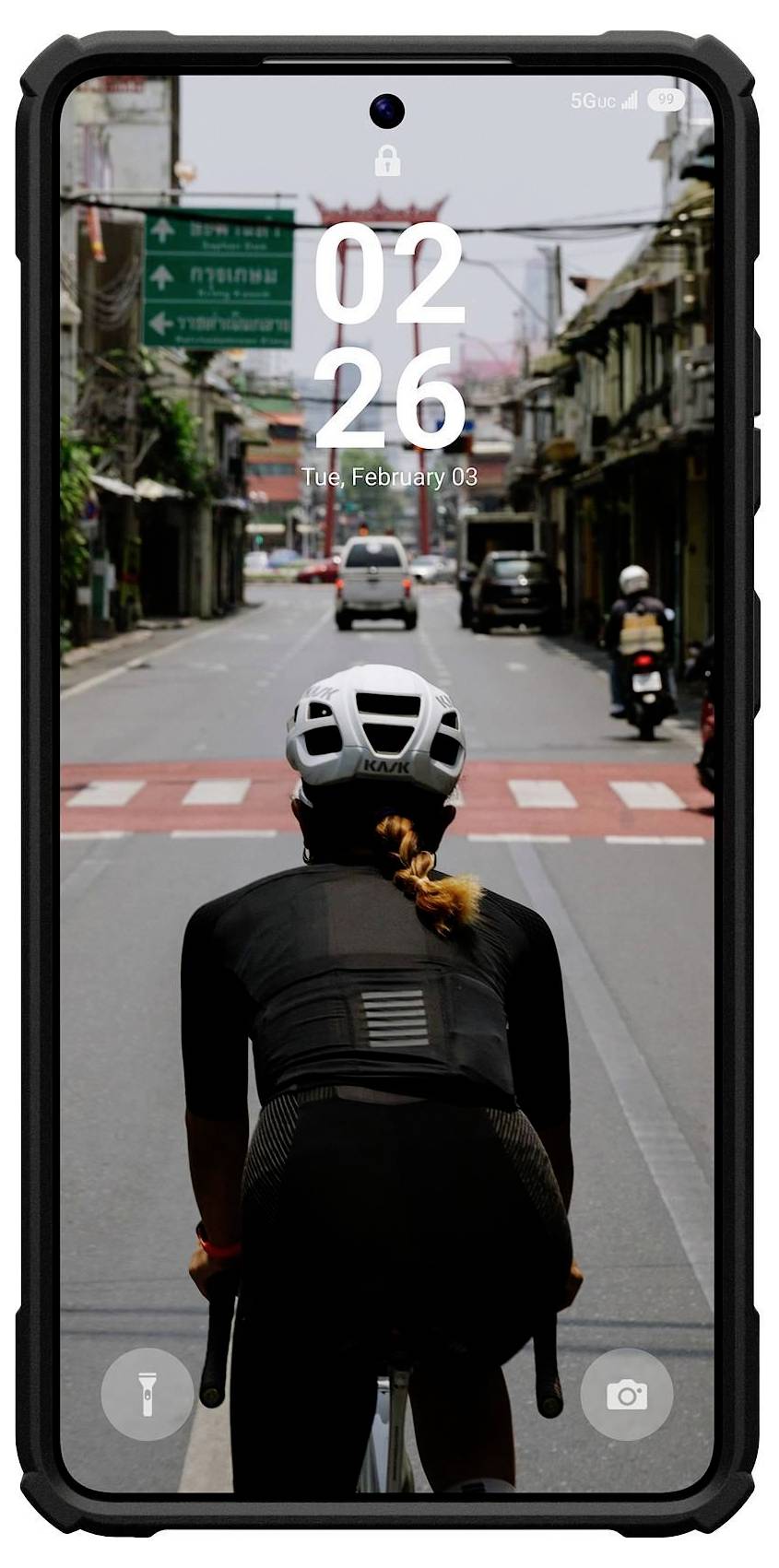 Ein Radfahrer mit Helm fährt auf eine Kreuzung in einer städtischen Straße zu, von hinten betrachtet. Die Telefonanzeige zeigt „02:26, Di., 3. Februar