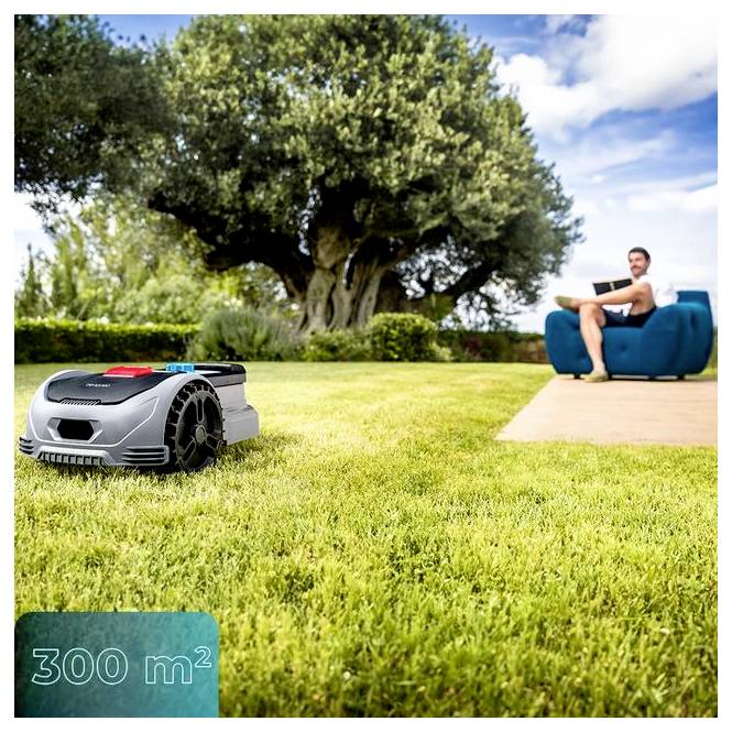 Ein Roboter-Rasenmäher ist auf einem grasbewachsenen Rasen neben einem großen Baum in Betrieb, während eine Person im Hintergrund auf einem Stuhl unter einem blauen Himmel sitzt.