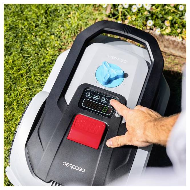Die Hand einer Person drückt einen Knopf auf dem Bedienfeld eines Roboter-Rasenmähers, der sich auf Gras befindet, mit Blumen im Hintergrund sichtbar.