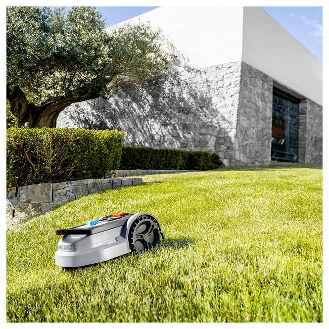 Ein Roboterrasenmäher auf frisch gemähtem Gras in der Nähe einer Steinmauer und eines Baumes unter klarem blauem Himmel, das automatisierte Rasenpflege veranschaulicht.