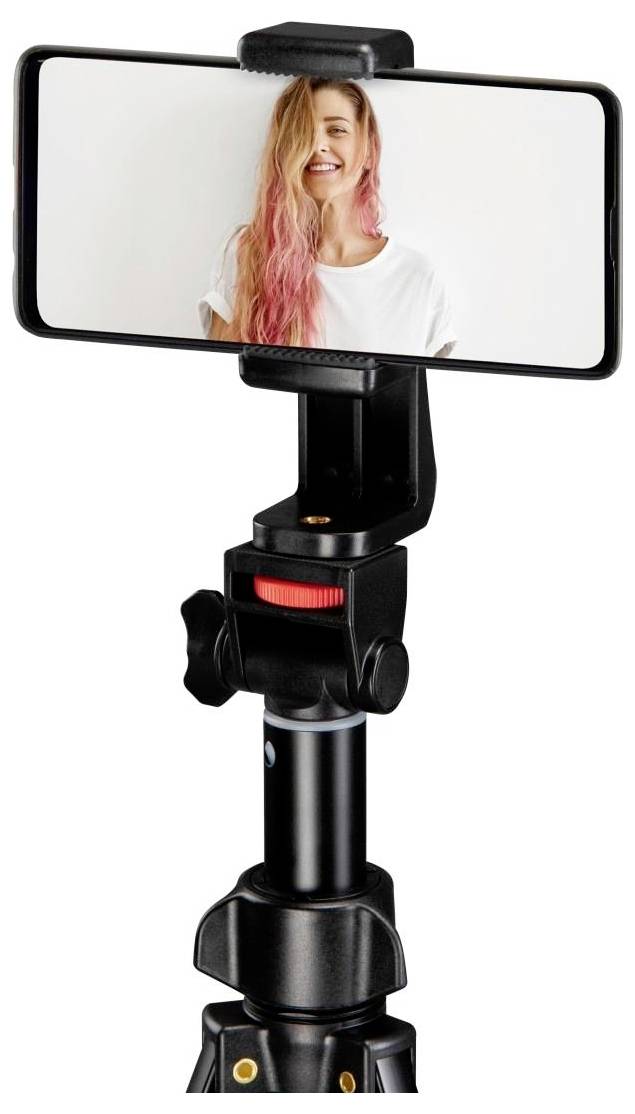 Ein auf einem Stativ montiertes Smartphone zeigt eine Person mit langen rosa Haaren, die lächelnd in die Kamera schaut, in einem gut beleuchteten Raum.