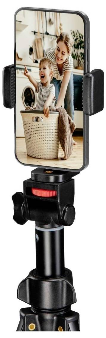 Ein Stativ hält ein Smartphone, das ein Foto eines lächelnden Kindes in einem Wäschekorb zeigt, mit einem Erwachsenen in der Nähe, in einer häuslichen Umgebung.