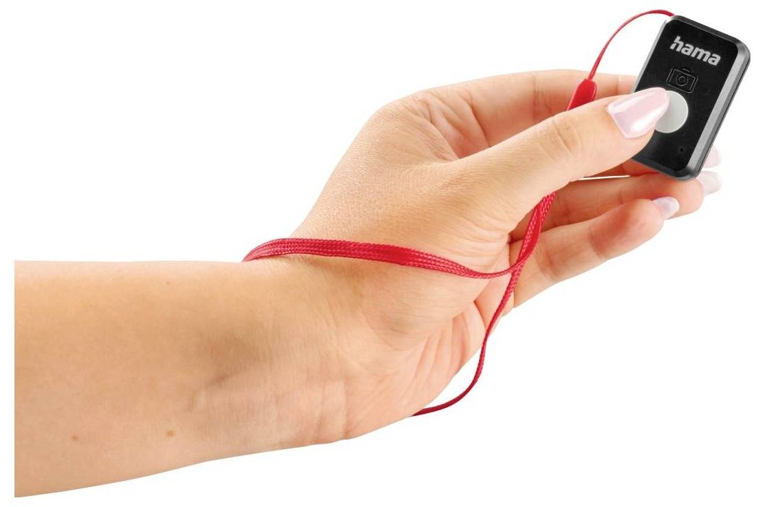 Eine Hand hält eine kleine, quadratische schwarze Fernbedienung mit einem roten Handgelenkband.