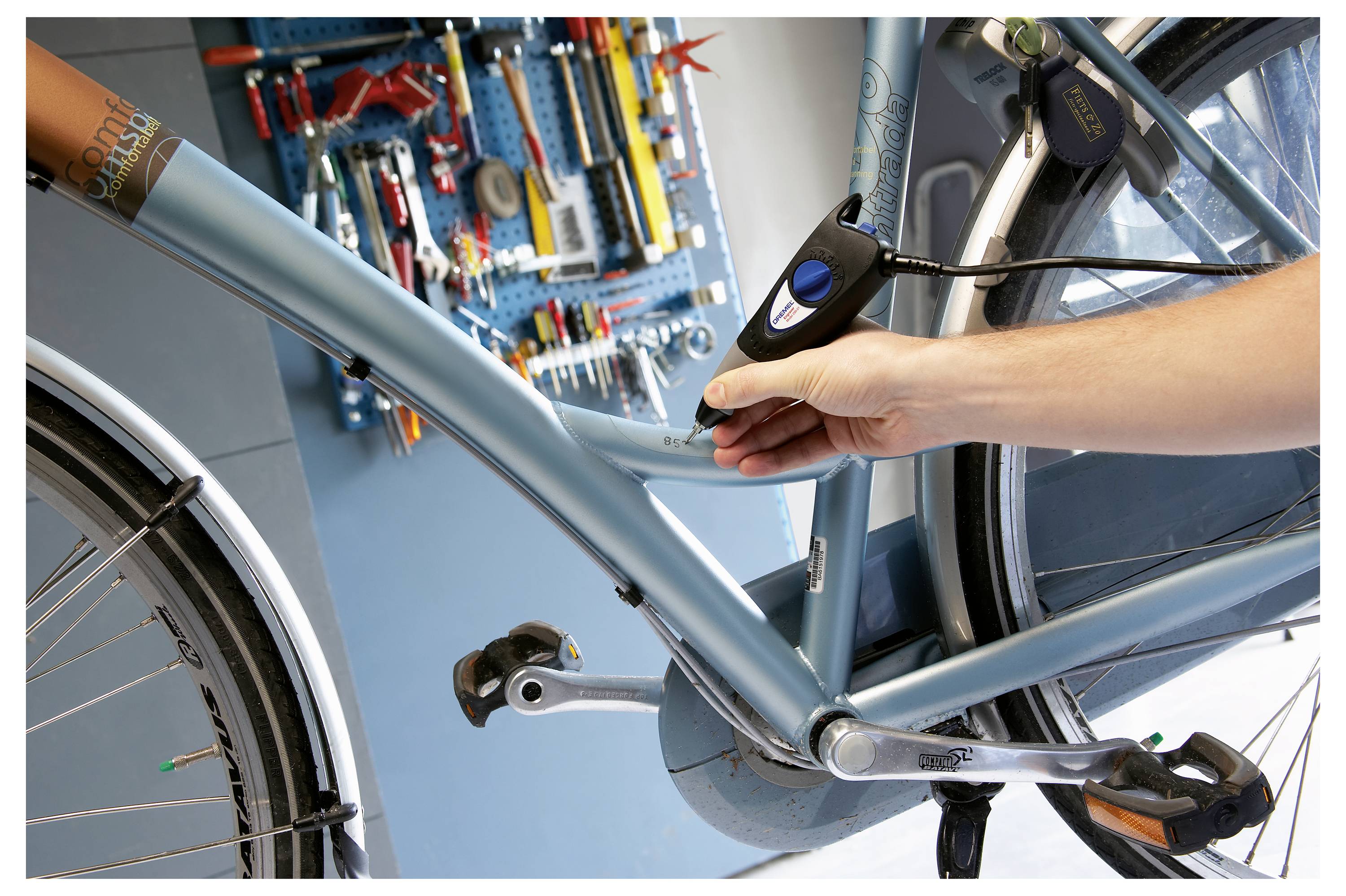 Eine Person bläst einen Fahrradreifen mit einer tragbaren Handpumpe auf, während verschiedene Werkzeuge auf einer wandmontieren Lochplatte im Hintergrund hängen.