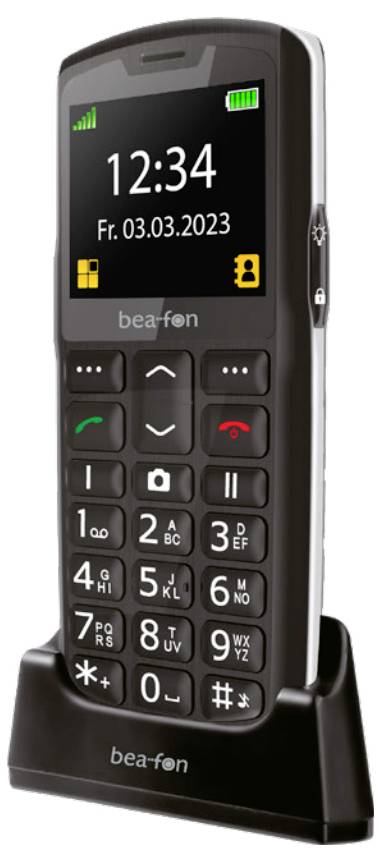 Ein schwarzes Mobiltelefon mit großen Tasten, einem kleinen Display, das '12:34' anzeigt, und dem Datum 'Fr. 03.03.2023', auf einer Ladestation platziert.