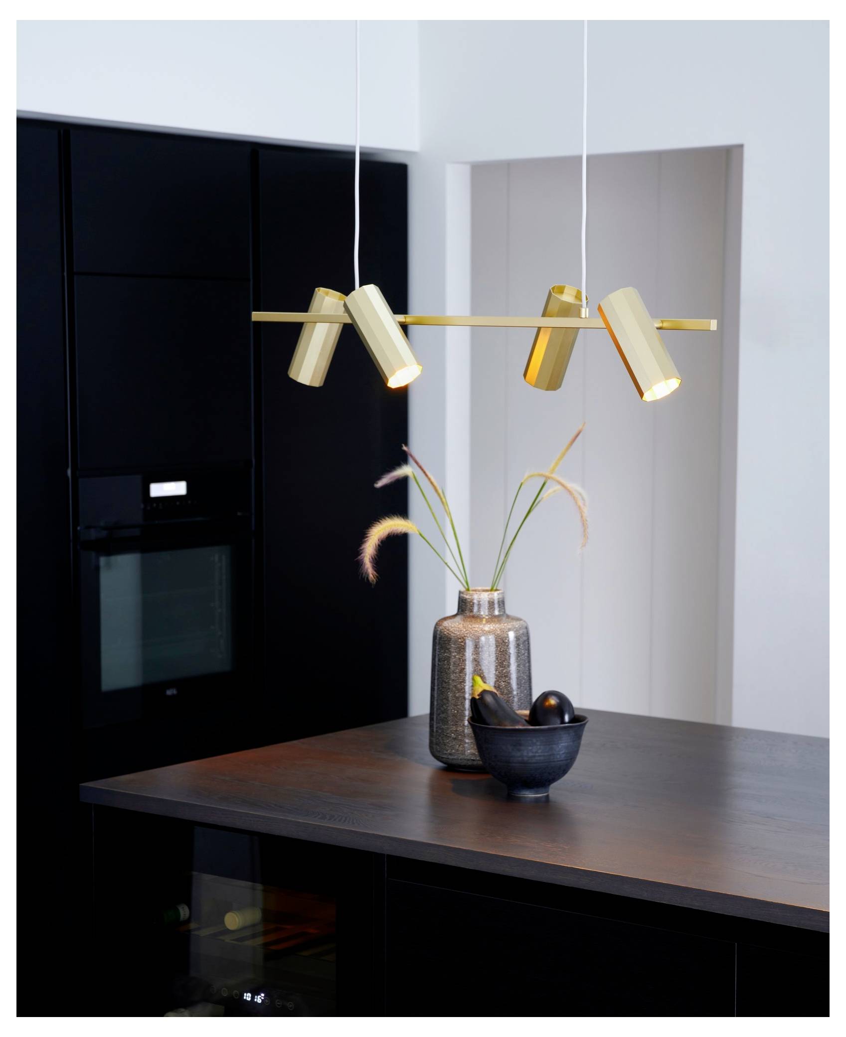 Eine moderne Küche mit einem eleganten schwarzen Ofen und einer Arbeitsplatte verfügt über eine goldene Pendelleuchte. Eine dekorative Vase mit Pflanzen und eine Schüssel stehen auf der Arbeitsplatte.