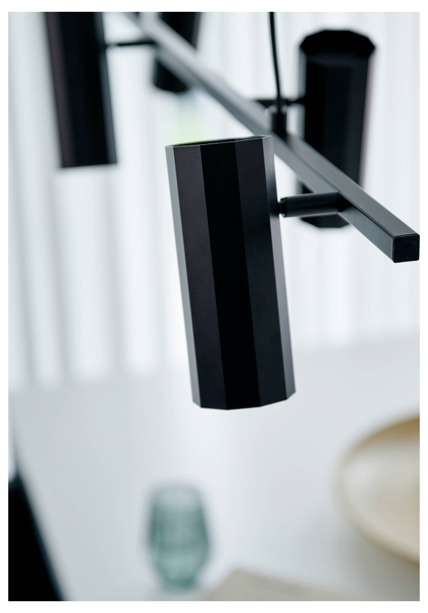 Nahaufnahme einer modernen schwarzen Deckenleuchte mit geometrischem Design, positioniert über einem unscharfen Esstischgedeck.