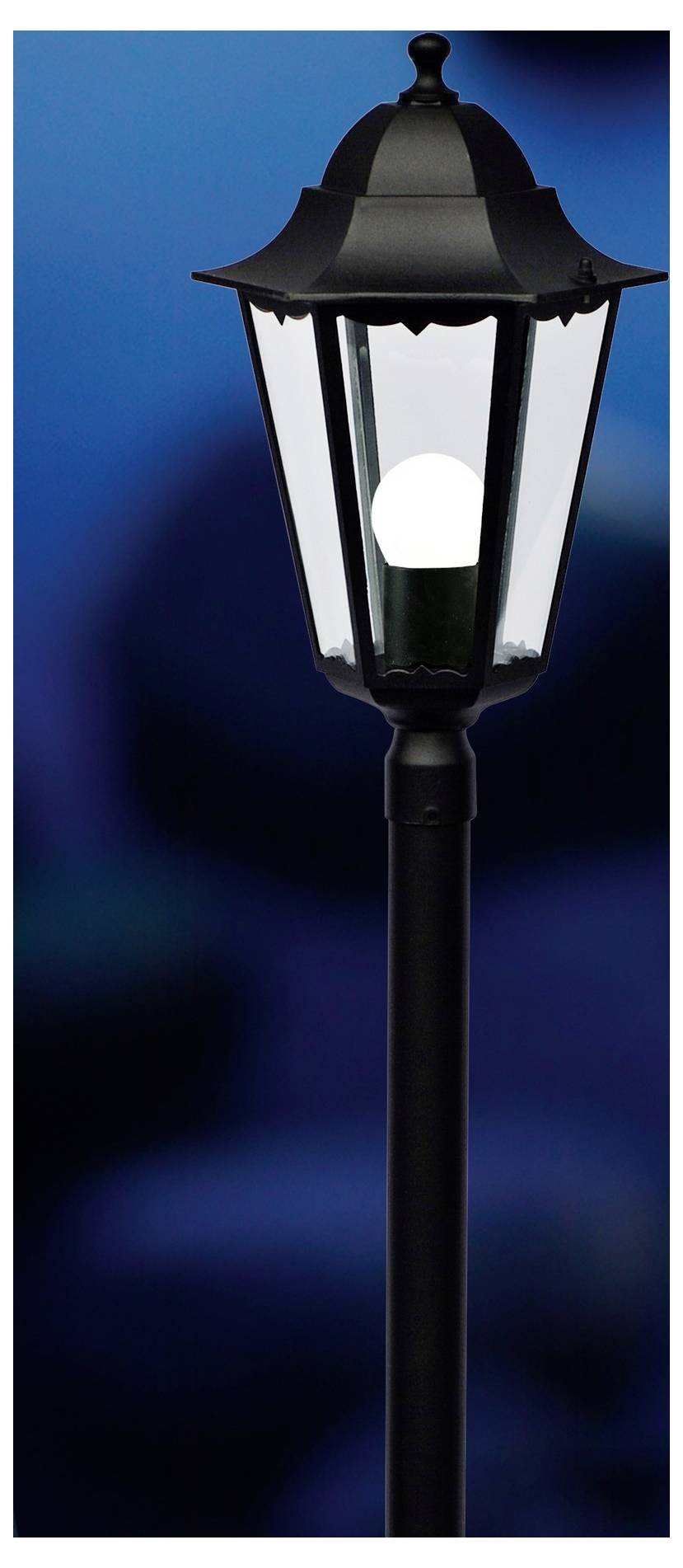 Ein schwarzer, traditioneller Lampenpfahl mit einer leuchtenden Glühbirne vor einem unscharfen blauen Hintergrund.