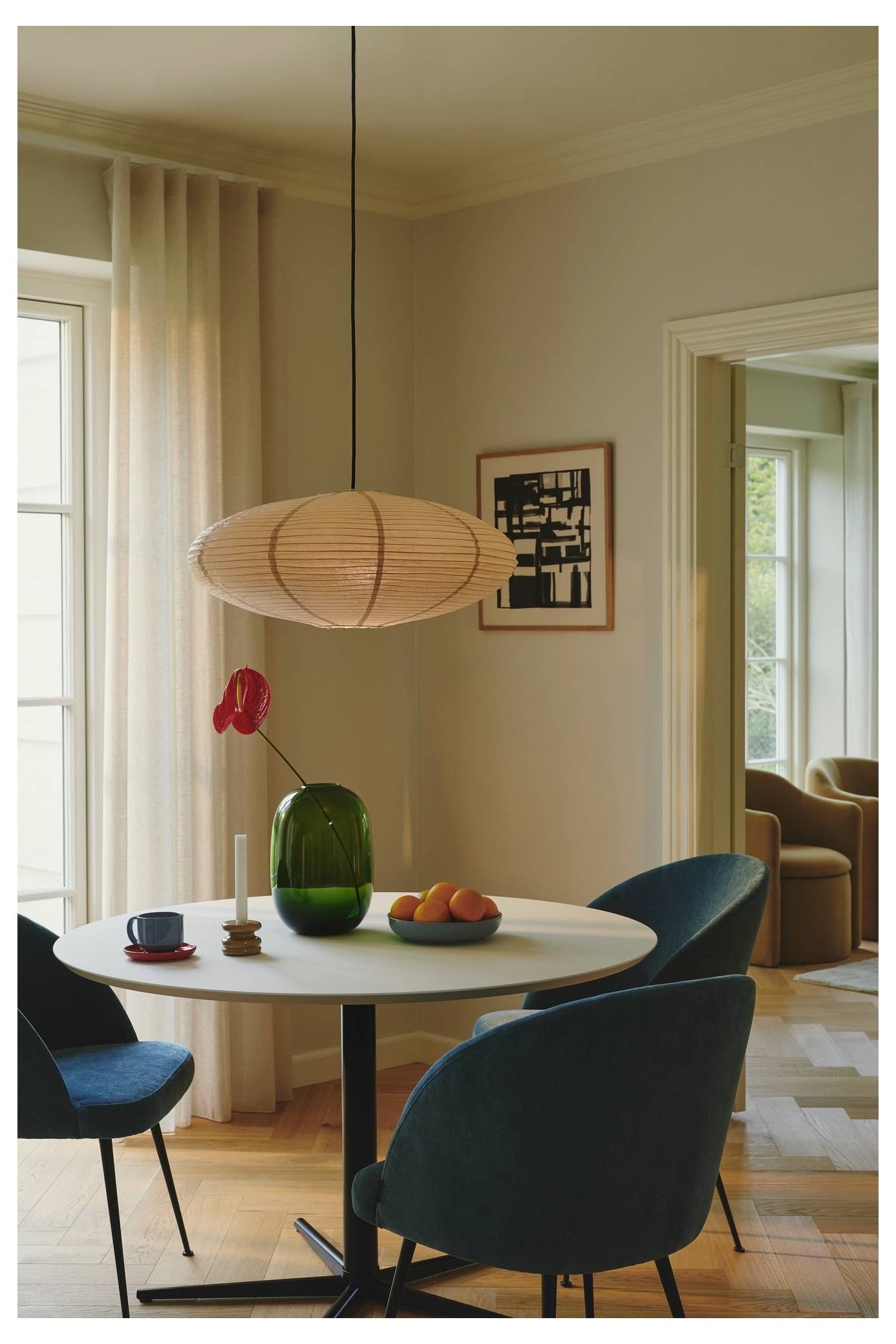 Ein moderner Essbereich mit einem runden Tisch, eleganten Stühlen, einer hängenden Leuchte und einer grünen Vase mit einer roten Blume, angeordnet neben einem Fenster.