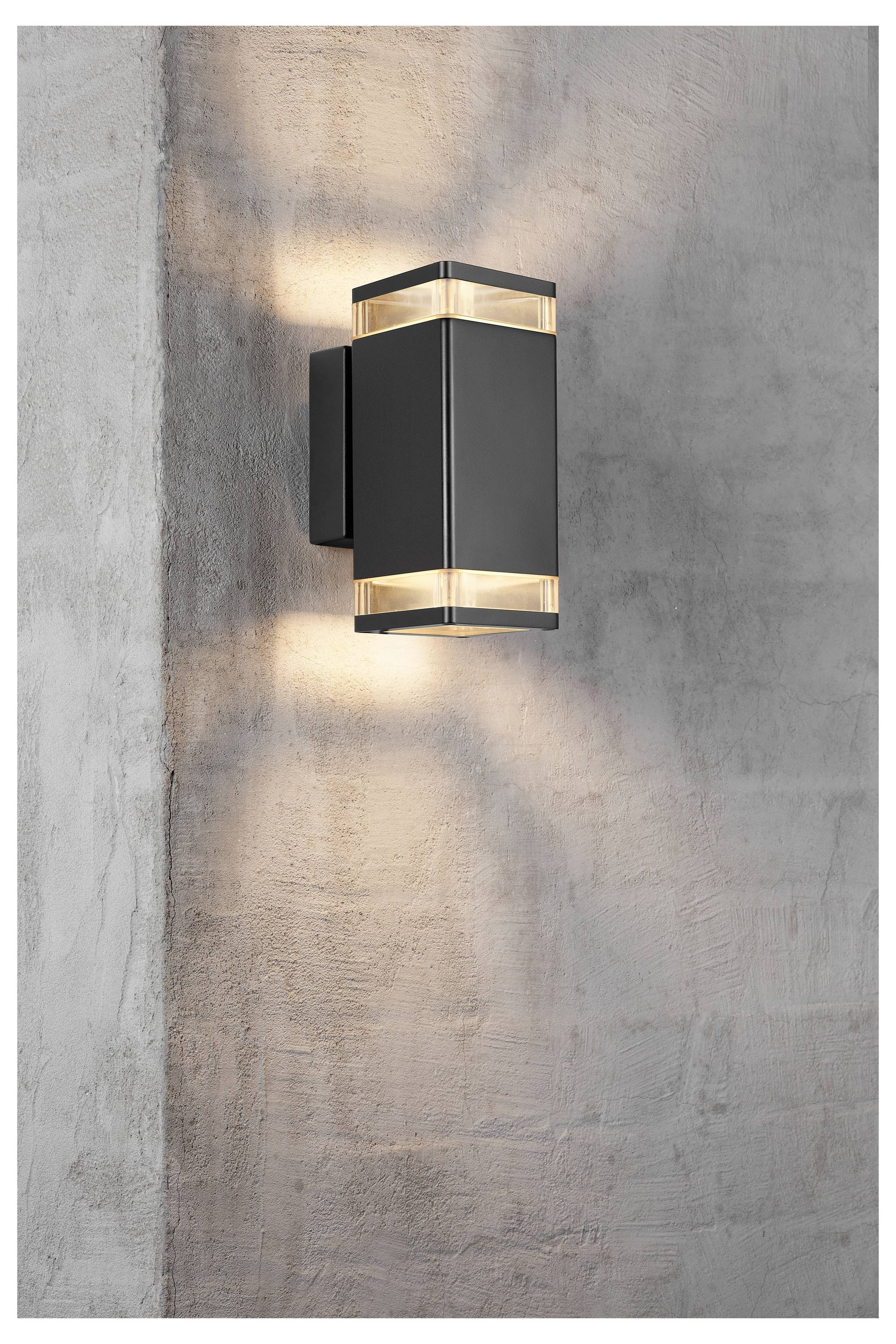 Eine moderne schwarze Wandleuchte, die an einer strukturierten grauen Wand montiert ist, spendet warmes Licht sowohl nach oben als auch nach unten und erzeugt weiche Schatten.