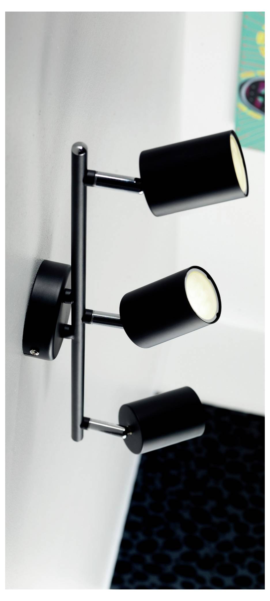 Drei schwarze Zylinder-Spotlights auf einer vertikalen Wandhalterung montiert, die eine nahegelegene Oberfläche beleuchten.