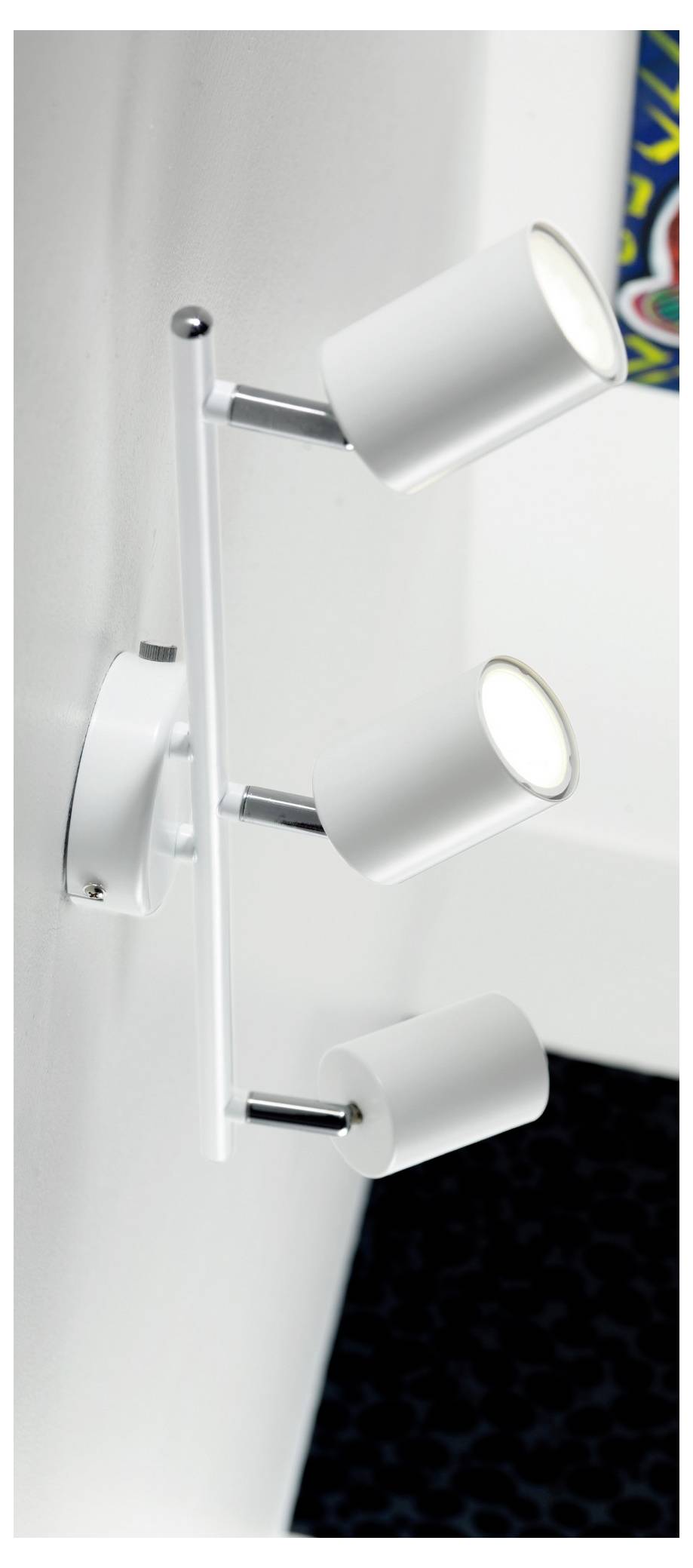 Weiße, an der Wand montierte dreifache Spotlightleuchte auf einem Chromhalter, in einer Raumecke positioniert mit einem Blick auf farbenfrohe Kunstwerke.