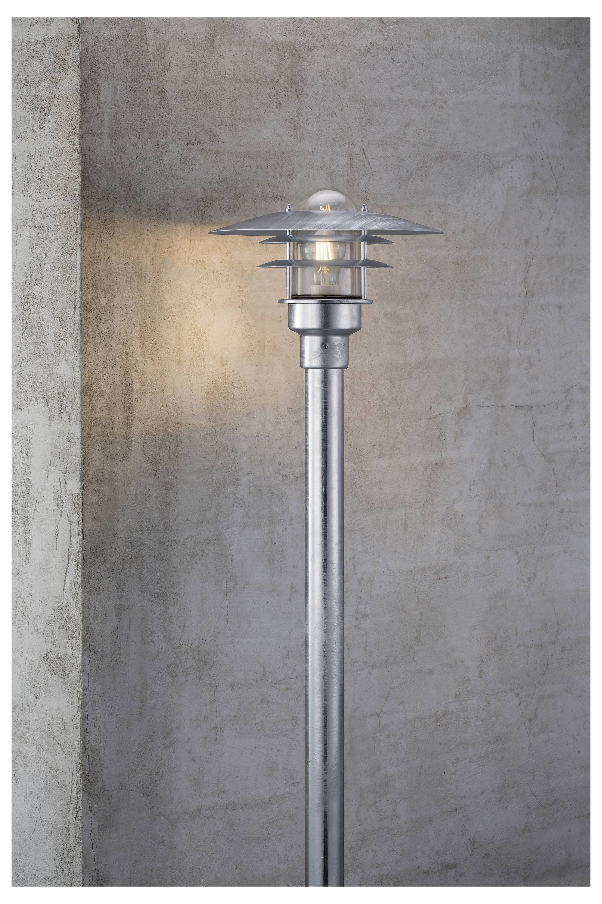 Eine moderne Außenwandleuchte mit metallischer Oberfläche an einer Betonwand montiert, die ein weiches, warmes Licht auf die Oberfläche wirft.