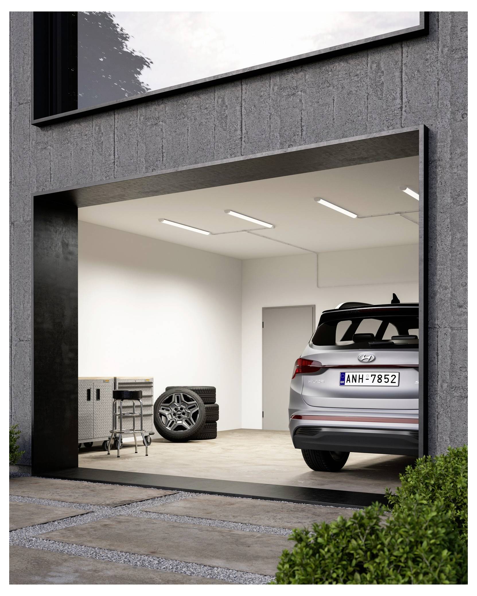 Ein grauer SUV steht in einer modernen, sauberen Garage mit einer Betongwand. Auf der linken Seite befinden sich eine Werkzeugkiste und ein Satz Ersatzreifen.