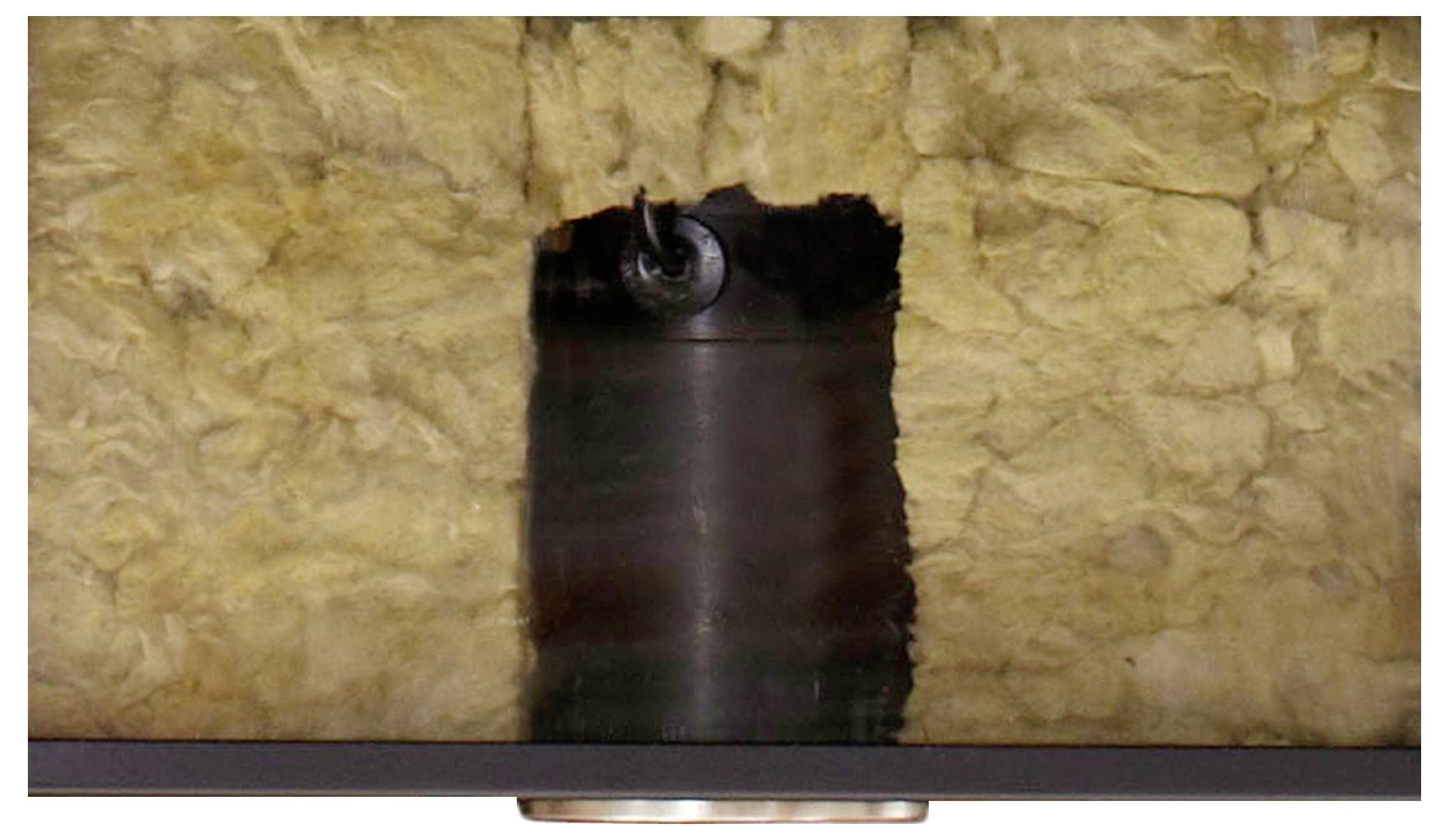 Ein vertikales Kupferrohr, umgeben von gelbem Isolationsmaterial an einer Decke, mit einer zylindrischen Leuchte in der Mitte unten.