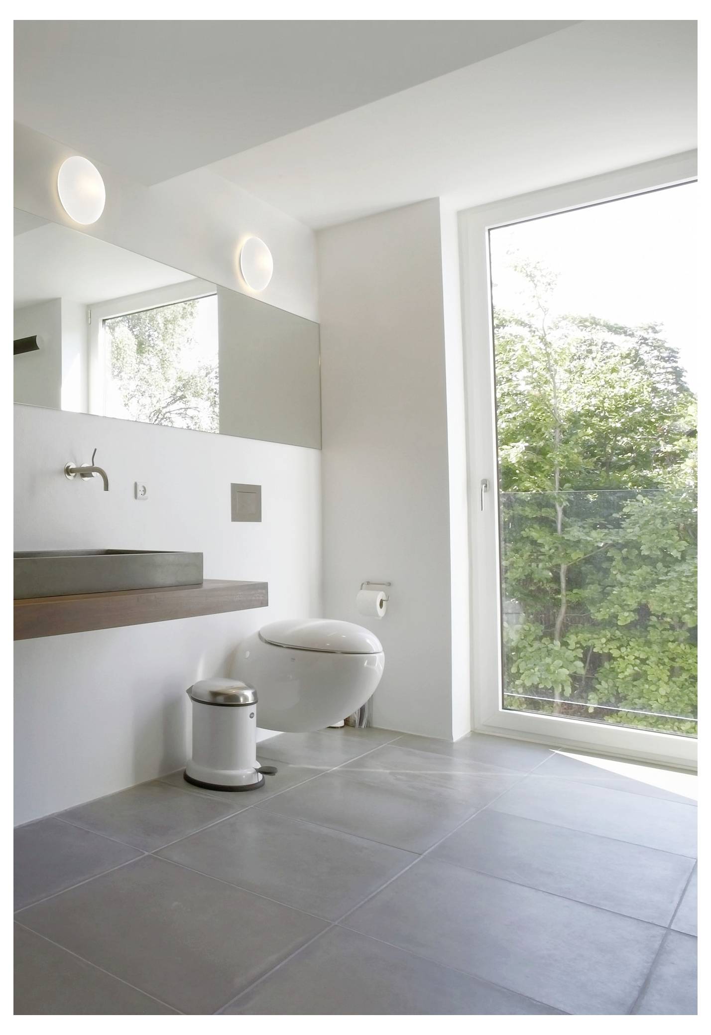Ein modernes Badezimmer mit einer weißen Toilette, einem rechteckigen Waschbecken, einem großen Fenster mit Ausblick auf Bäume und minimalistischer Einrichtung.
