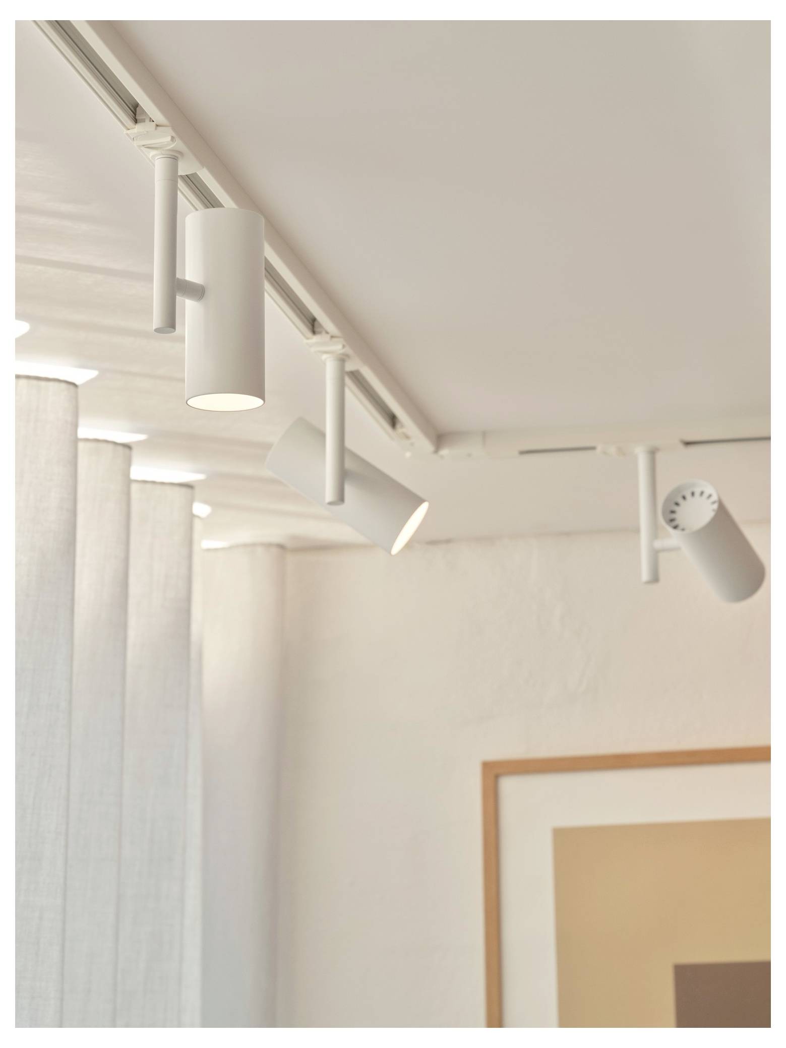 Deckenmontageleuchte mit verstellbaren zylindrischen Leuchten in einem minimalistischen Raum, die ein abstraktes gerahmtes Kunstwerk hervorhebt.