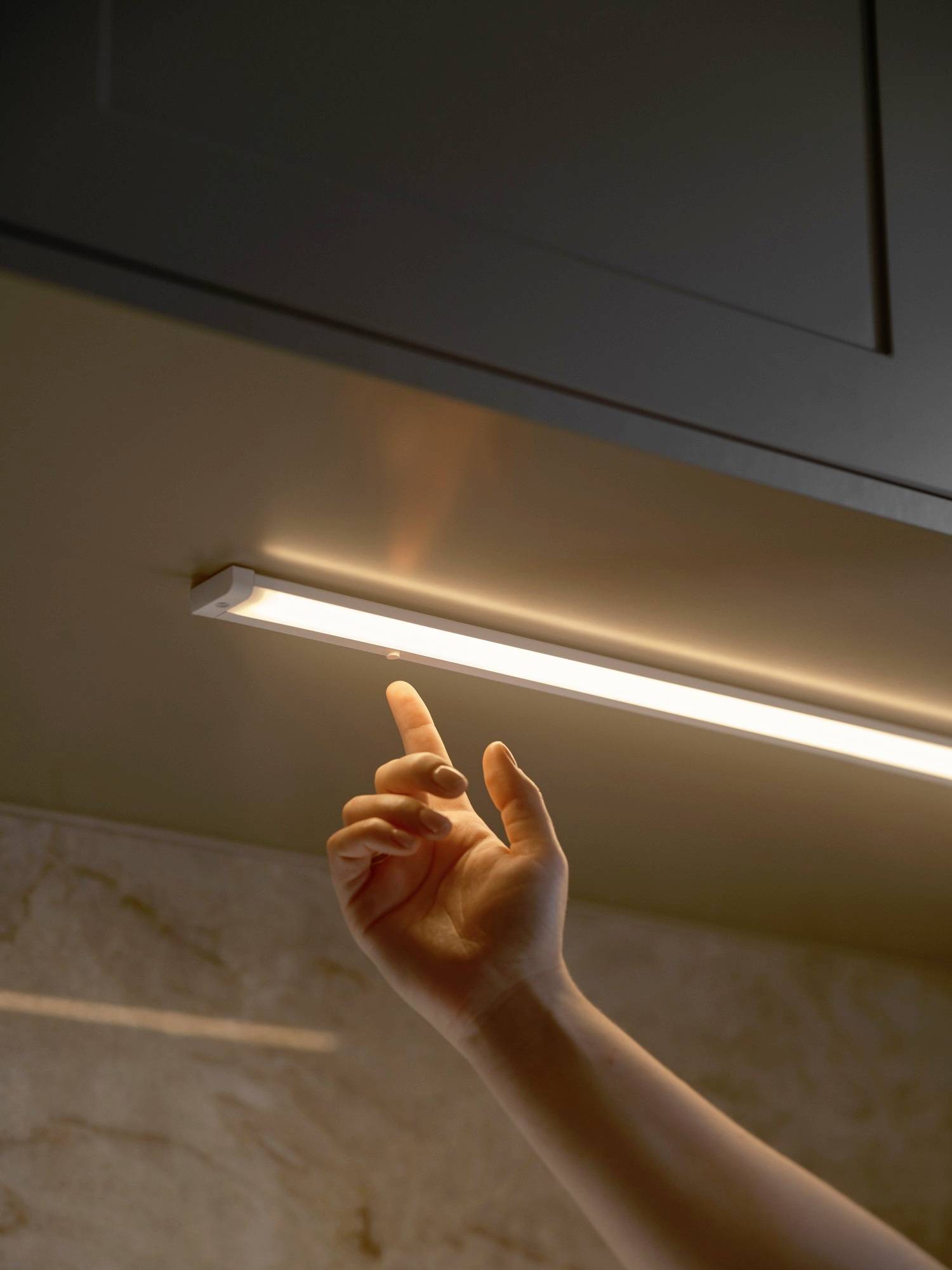 Eine Hand, die einen LED-Leuchten-Schalter unter der Küchenschrank-Beleuchtung betätigt, in einer Küchenumgebung.